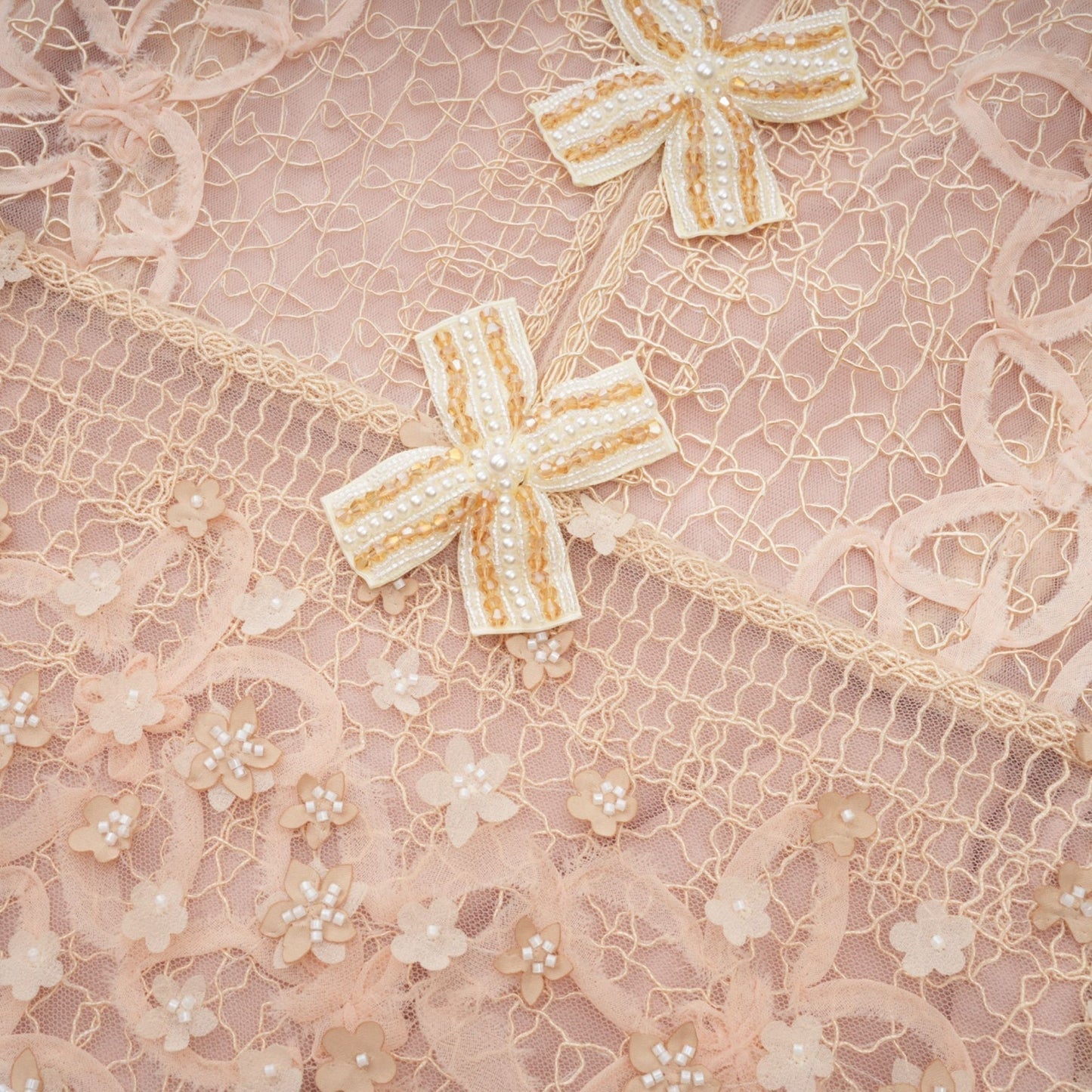 A beige midi dress with a crochet pattern and faux flower embellishments worn by a model standing against a neutral background