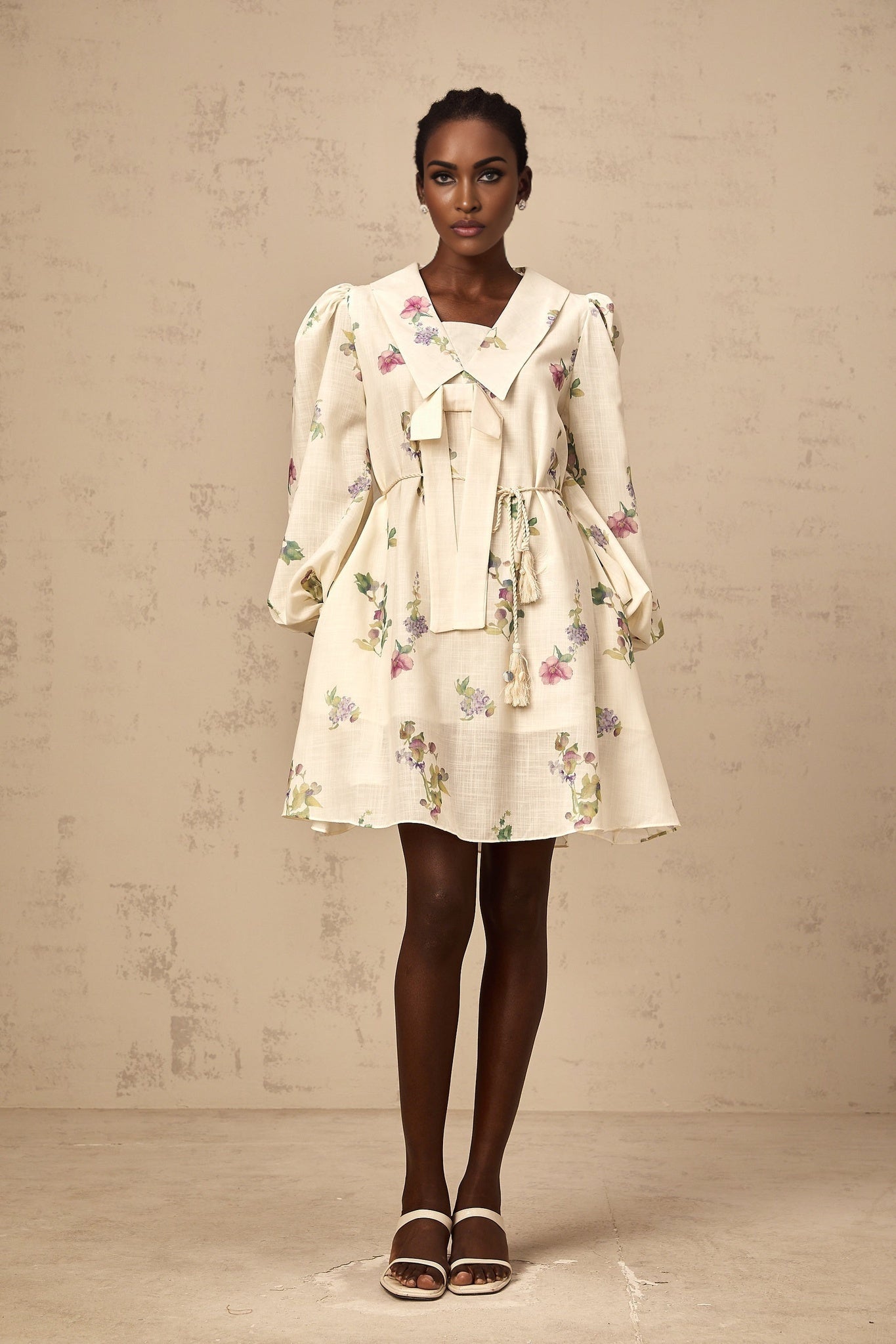 A beige mini dress with a floral print pattern and a decorative bow detail at the waist