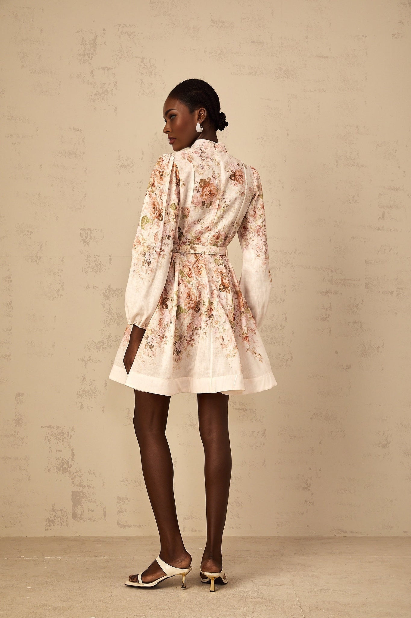 A beige mini dress with floral print pattern worn by a female model standing against a plain background
