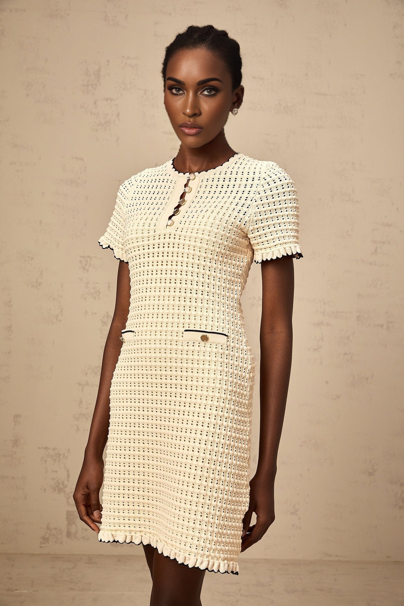 A beige mini dress with ruffled details and pointelle knit texture featuring a fitted bodice and short skirt