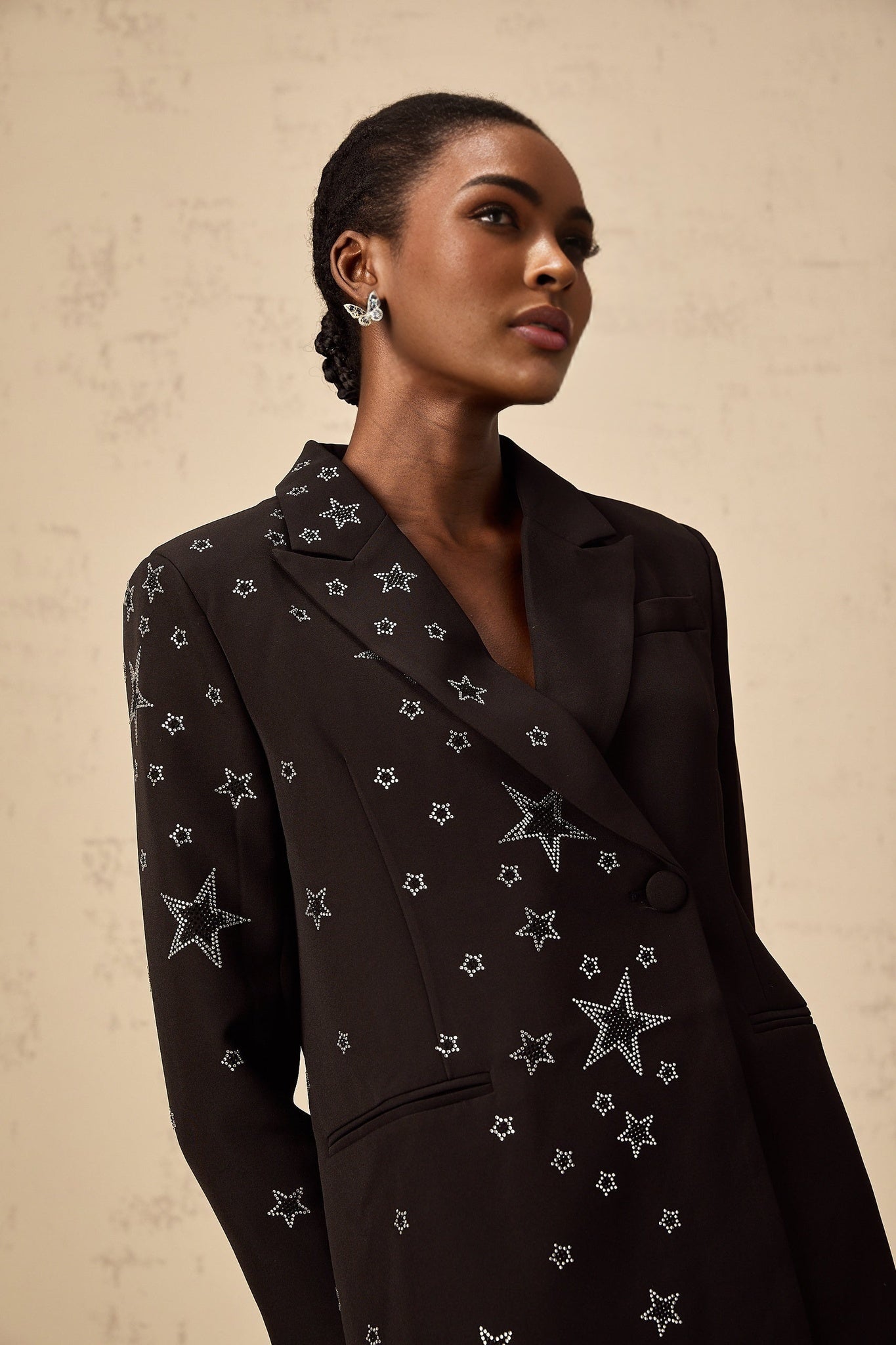 A black blazer with star appliques featuring a tailored fit and long sleeves worn by a model against a plain background