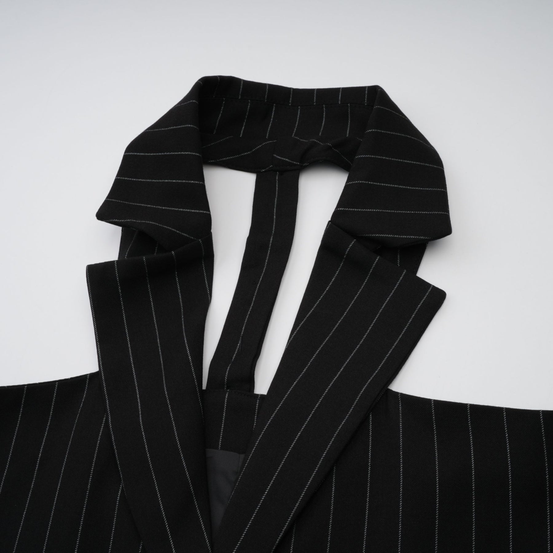 A black blazer with white stripes featuring an open back design worn by a model facing away from the camera