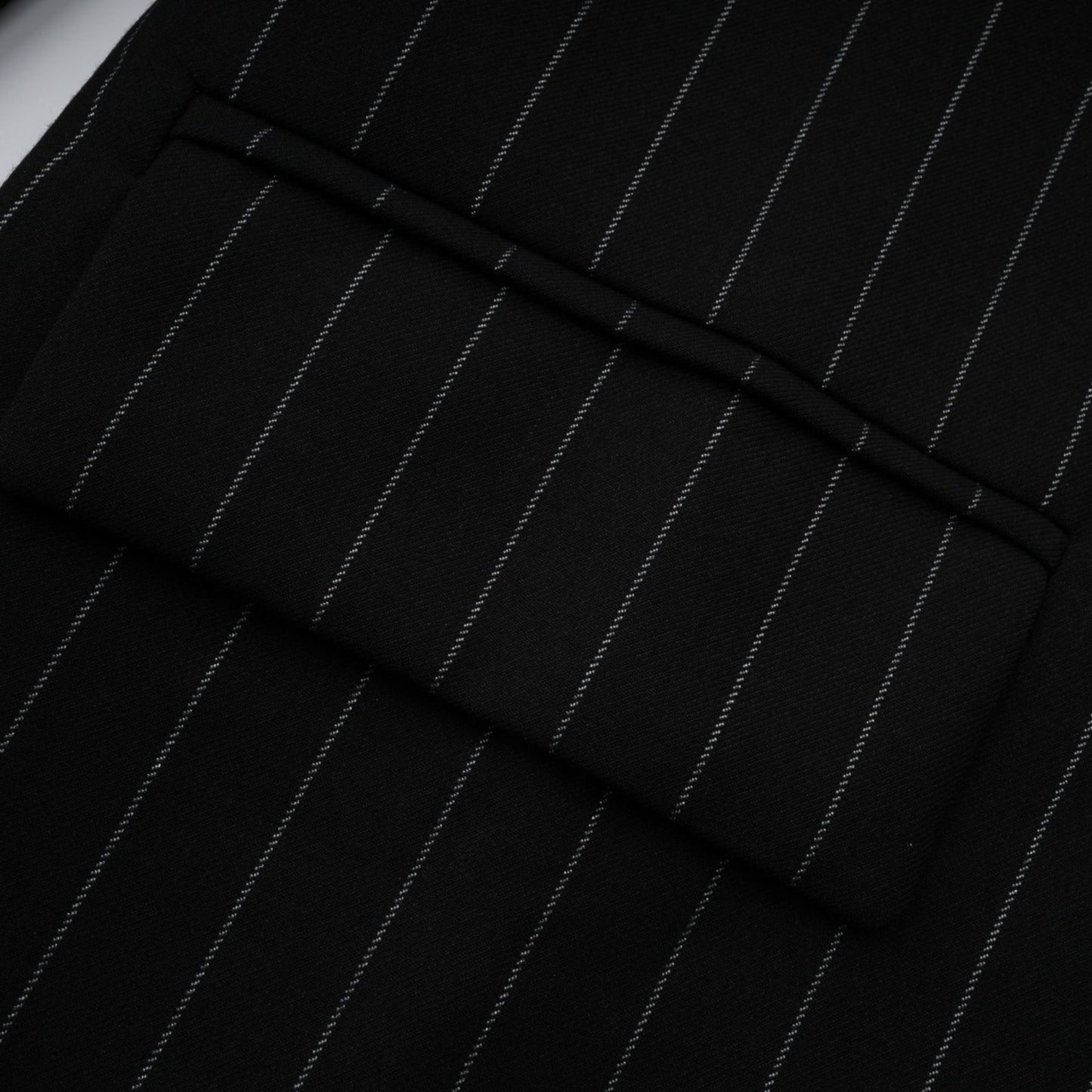 A black blazer with white stripes featuring an open back design worn by a model facing away from the camera