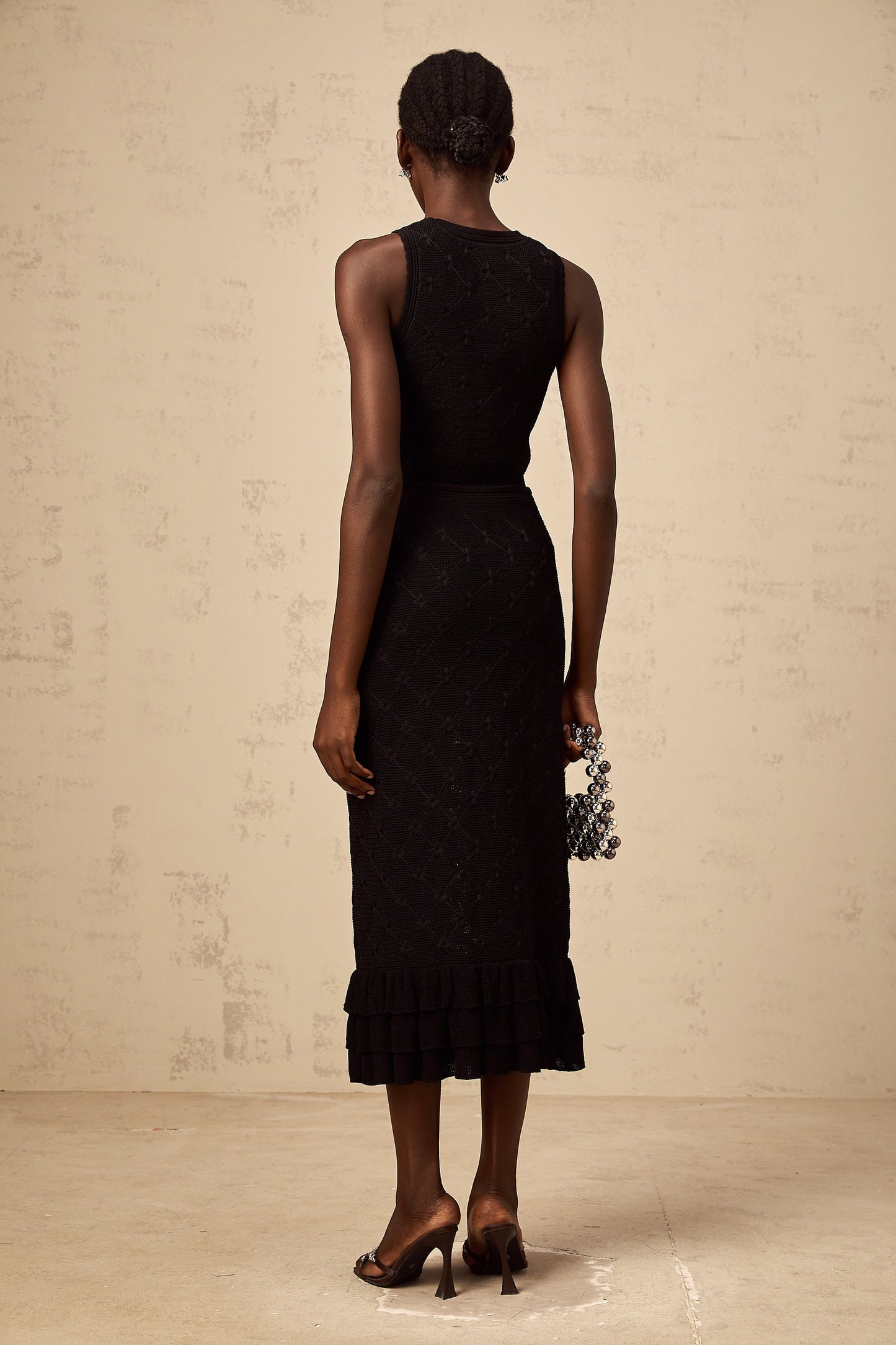 A black crochet knit matching set consisting of a top and skirt The top is sleeveless with a cropped length The skirt is fitted and falls to about knee length Both pieces feature an intricate crochet pattern throughout