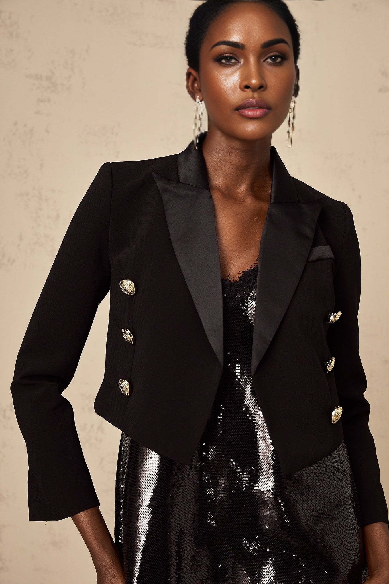 A black cropped blazer with double breasted front styled on a model against a plain background