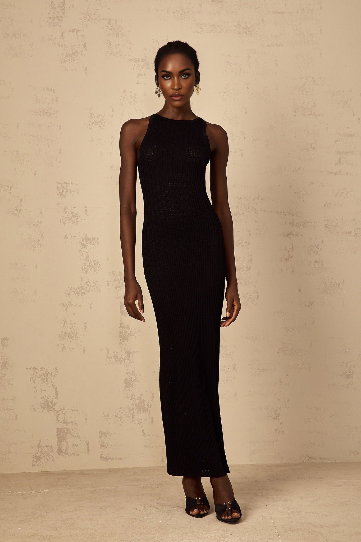 A black fitted ribbed knit maxi dress with long sleeves and a form fitting silhouette extending to the ankles