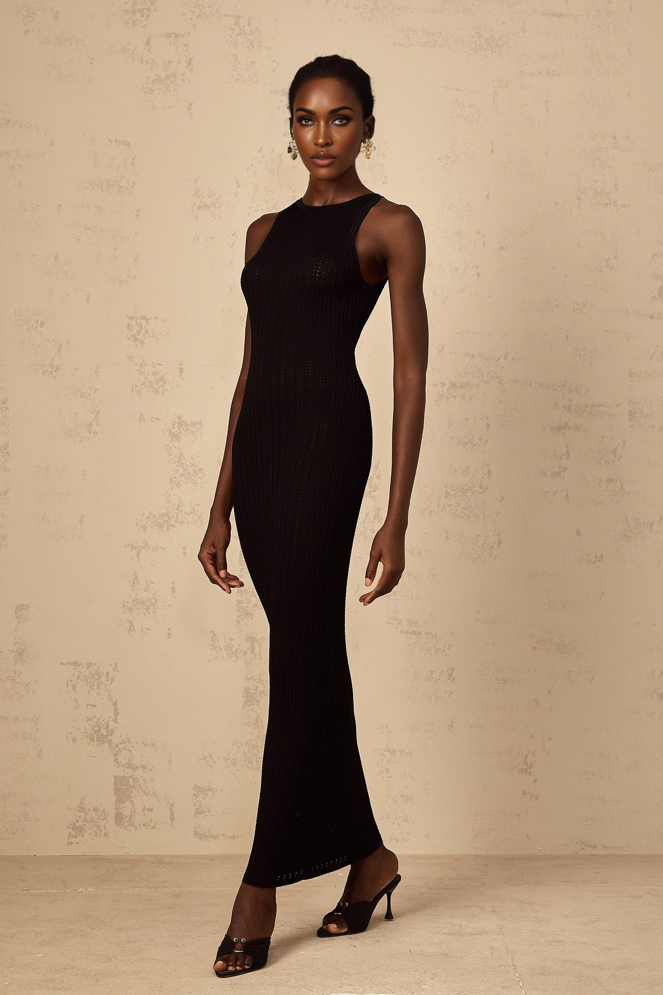 A black fitted ribbed knit maxi dress worn by a model standing against a plain background