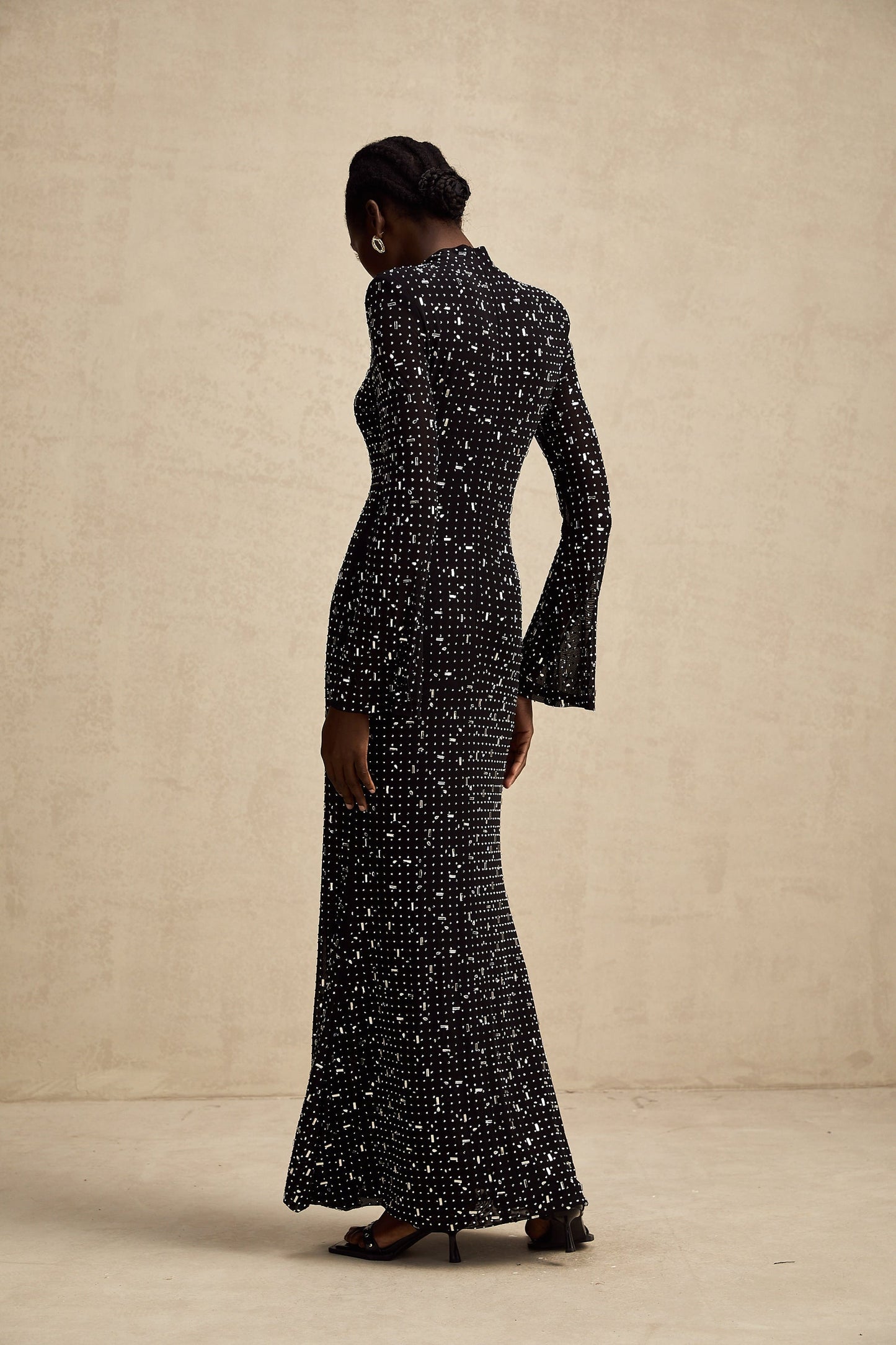 A black floor length maxi dress with sheer fabric and embellished details worn by a model standing against a plain background