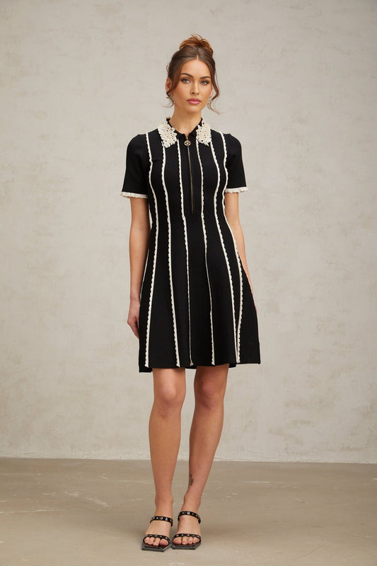 A black knit mini dress with vertical white stripes and ruffle trim details on a female model
