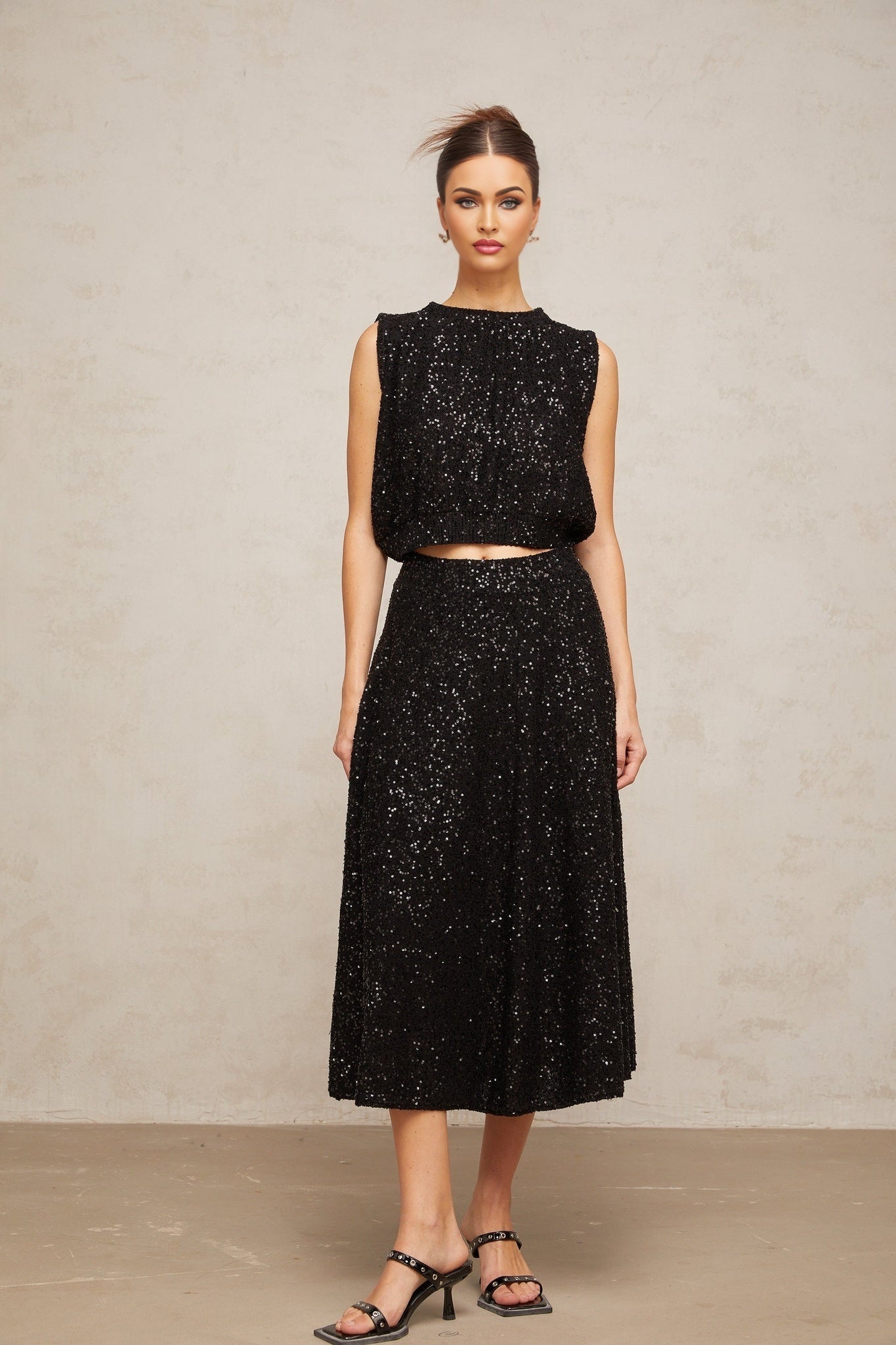 A black knit vest and skirt set adorned with sequins creating a shimmering effect Both pieces feature a matching sequined pattern The vest is sleeveless and the skirt appears to be knee length Together they form a coordinated and elegant outfit
