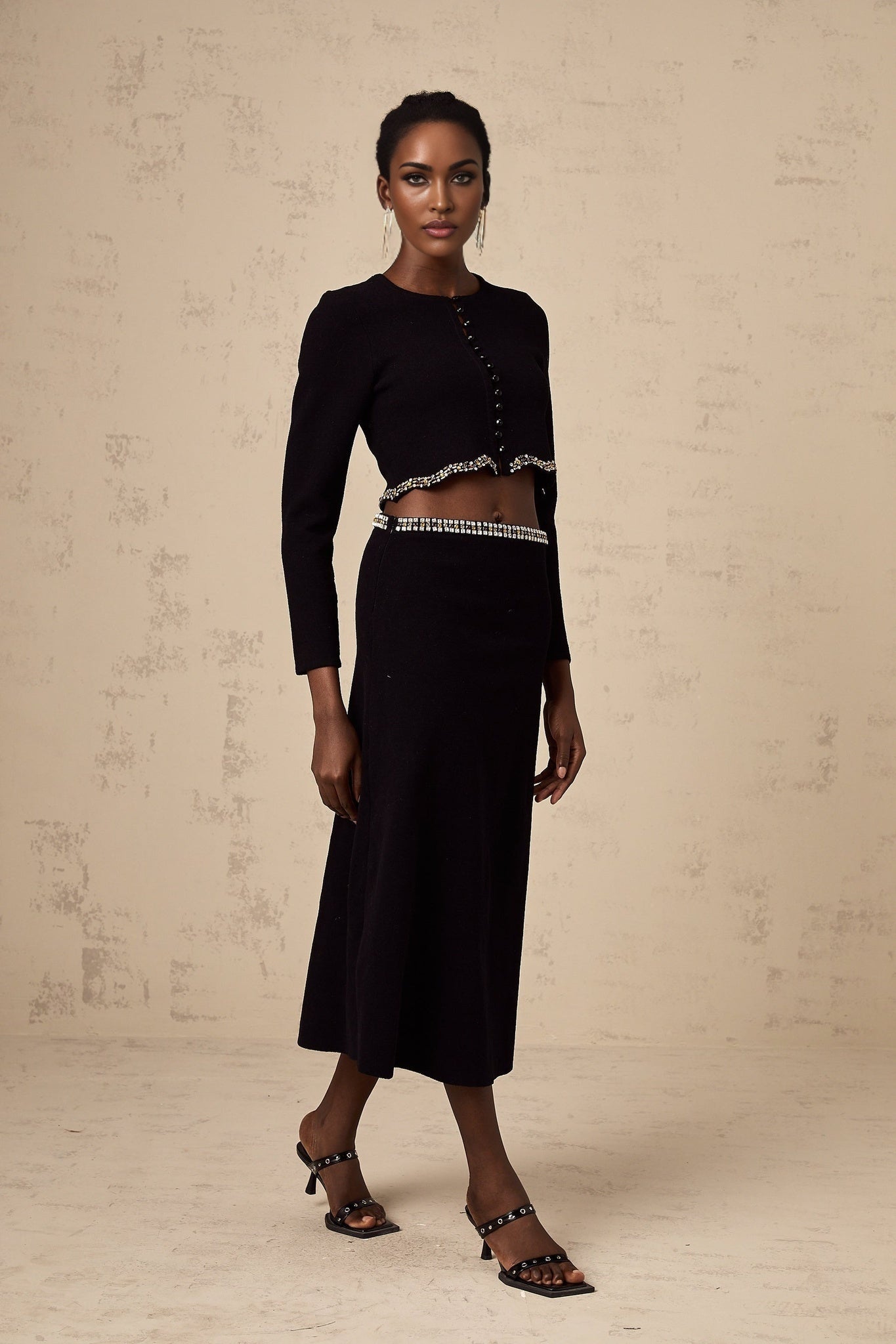 A black knitted matching set consisting of a cardigan and skirt The cardigan features embellishments and both pieces are styled together on a model