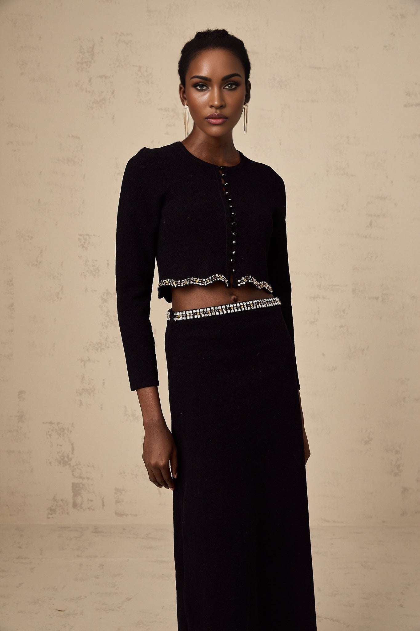 A black knitted matching set featuring a cardigan and skirt with embellished details The cardigan has long sleeves and the skirt is knee length Both pieces are adorned with decorative elements creating an elegant coordinated outfit