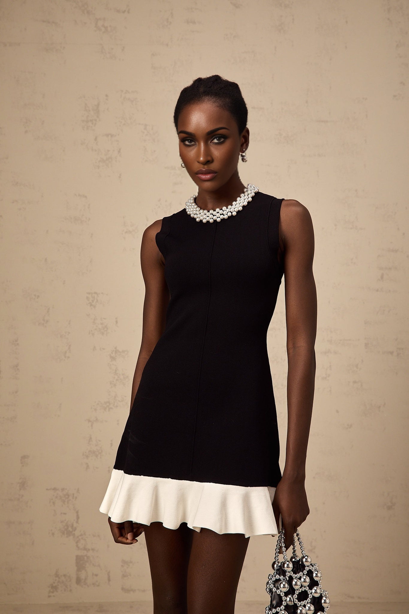 A black knitted mini dress with ruffled details and faux pearl embellishments featuring a short hemline and fitted silhouette