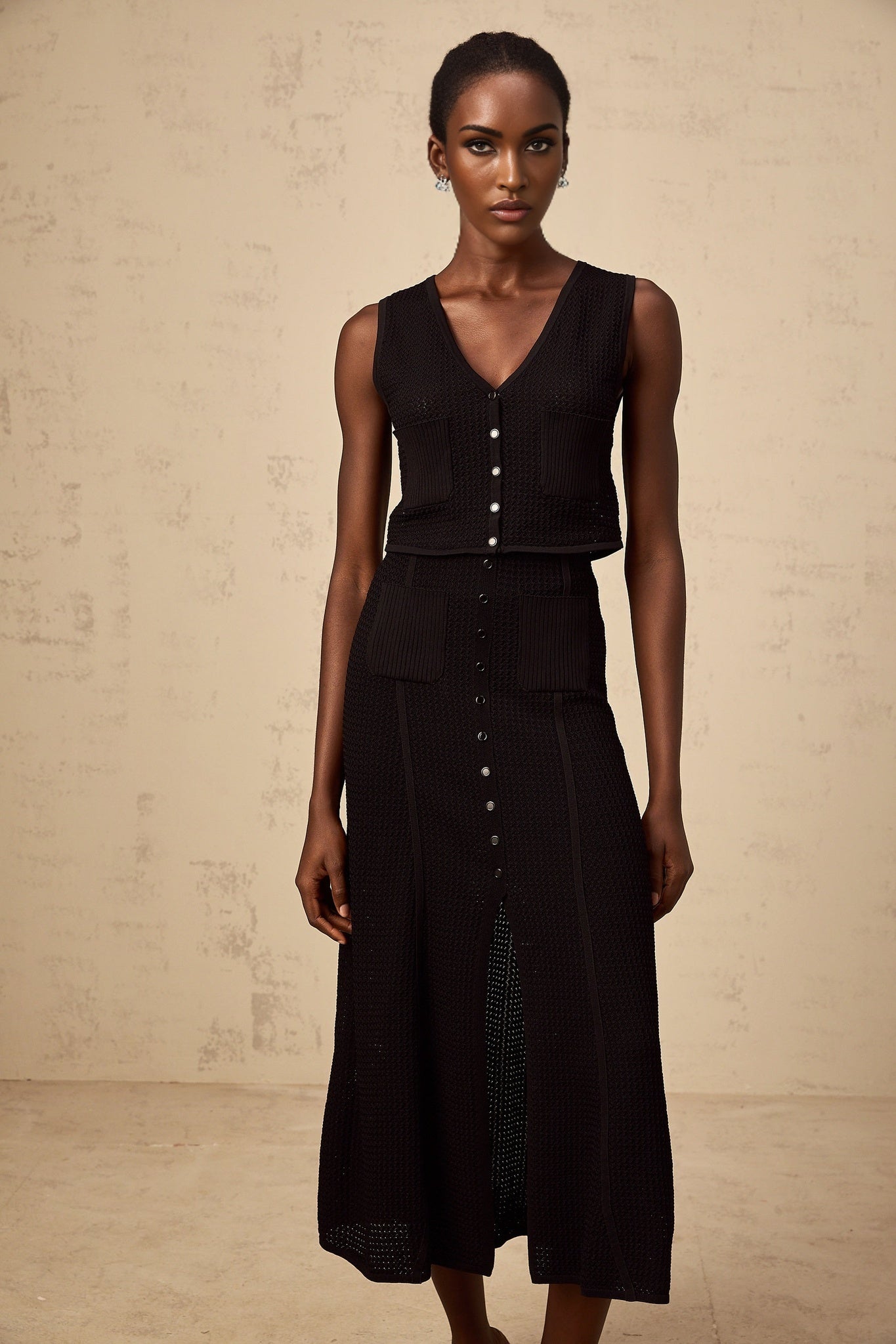 A black matching set consisting of a pointelleknit top and skirt named Babette The top and skirt feature a delicate knit pattern with small holes throughout creating a light and airy texture