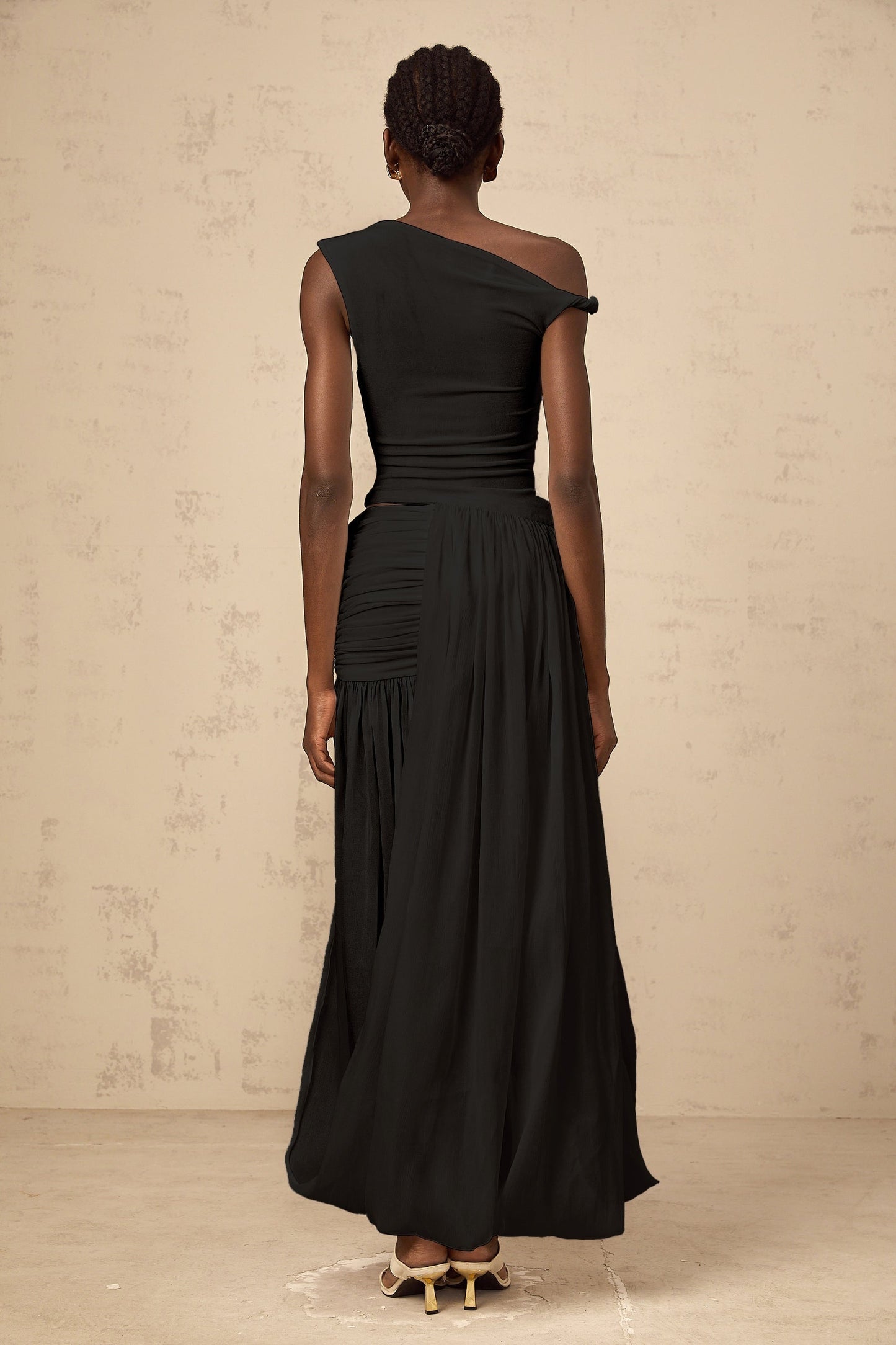 A black maxi dress with a single shoulder strap and shirred panels along the body featuring a sleek and elegant design