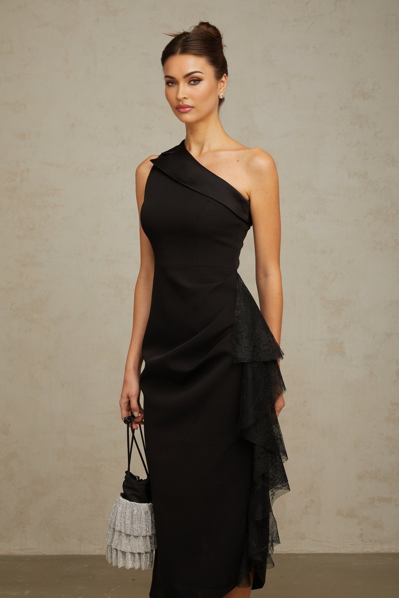 A black midi dress with asymmetric hemline featuring lace panels worn by a model standing against a plain background