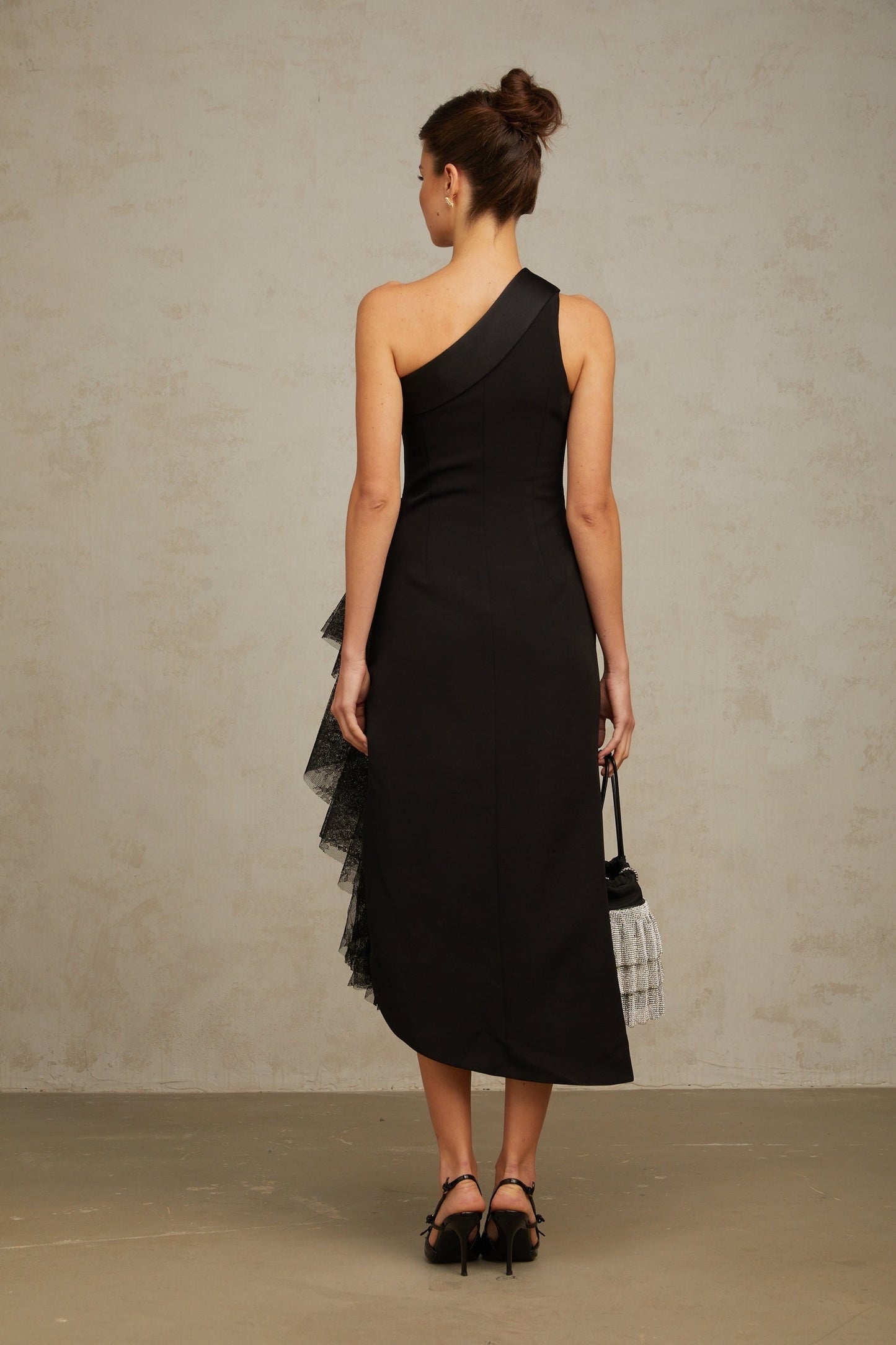 A black midi dress with lace panels and an asymmetric hemline worn by a model standing against a plain background