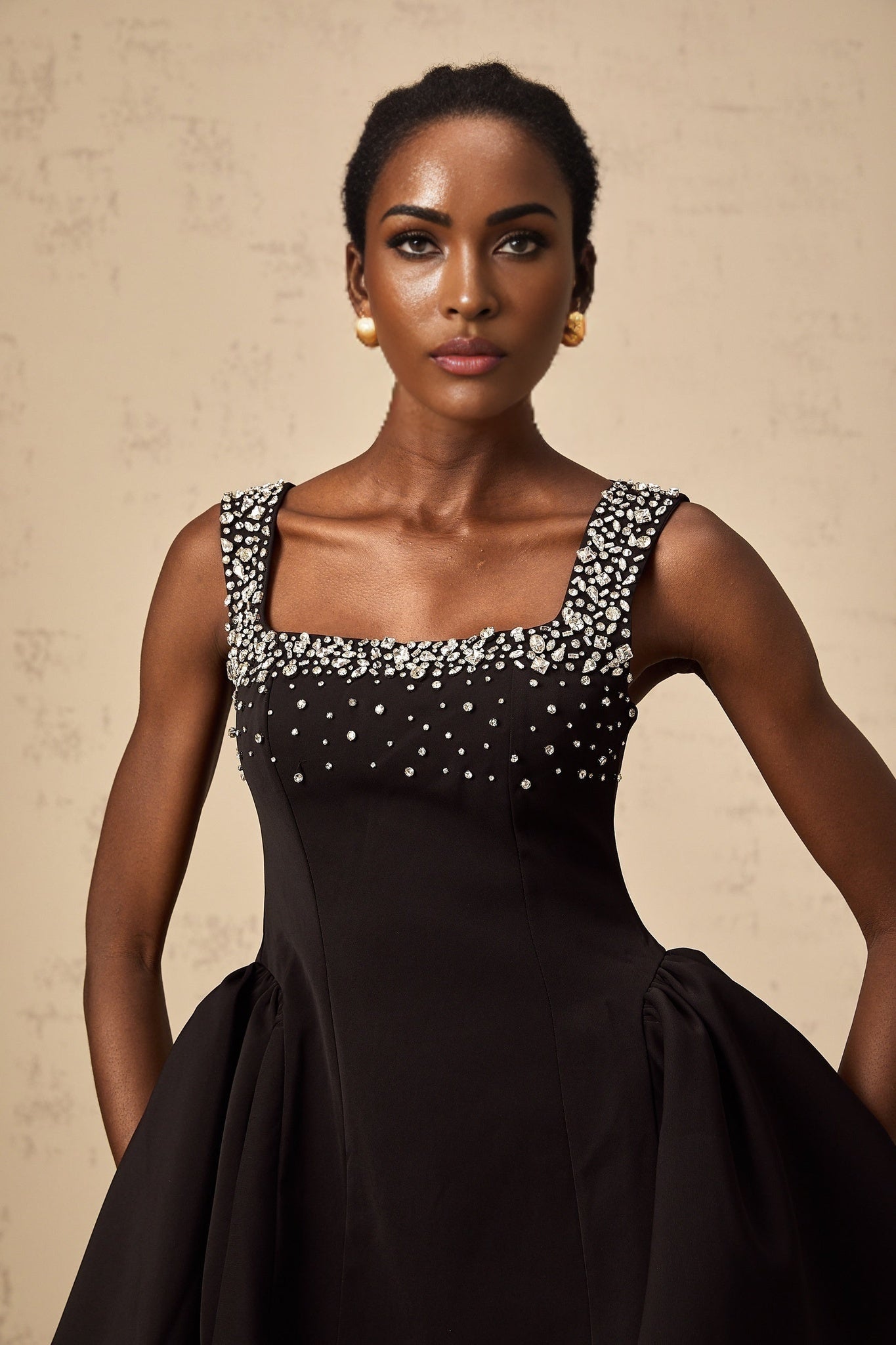 A black mini dress with a flared skirt and crystal embellishments worn by a model against a plain background