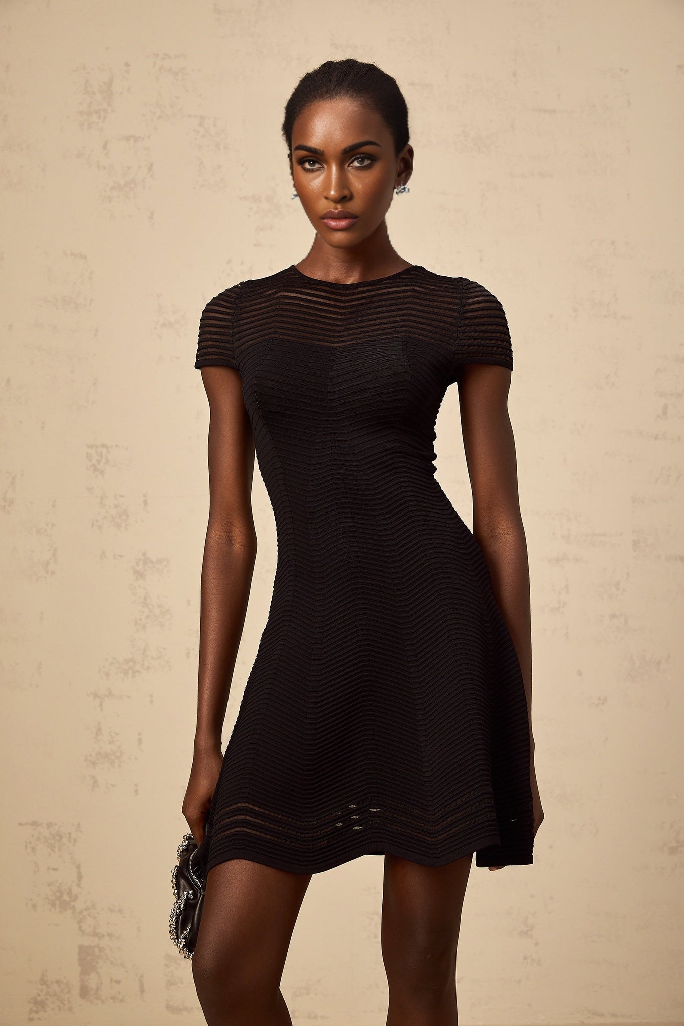 A black mini dress with a wavy crochet texture featuring a formfitting silhouette and intricate textured pattern throughout