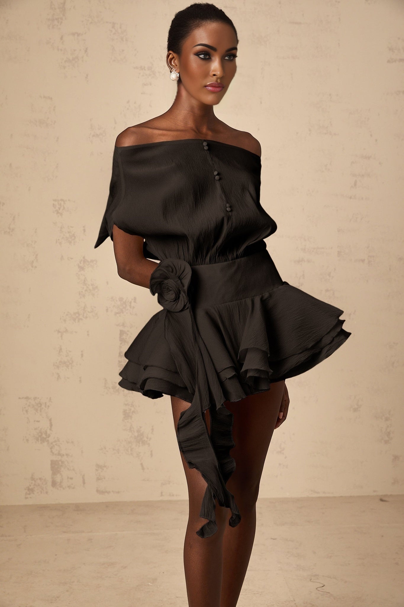 A black mini dress with floral applique detailing and a flounced hem worn by a woman named Amelie
