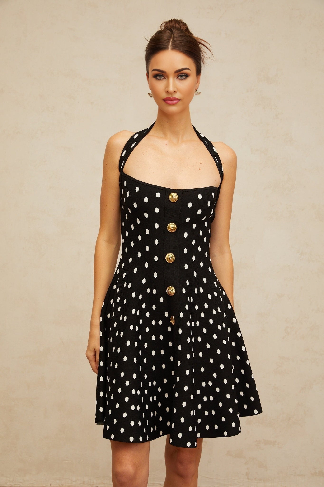 A black mini dress with white polka dots and a knit texture worn by a model against a plain background