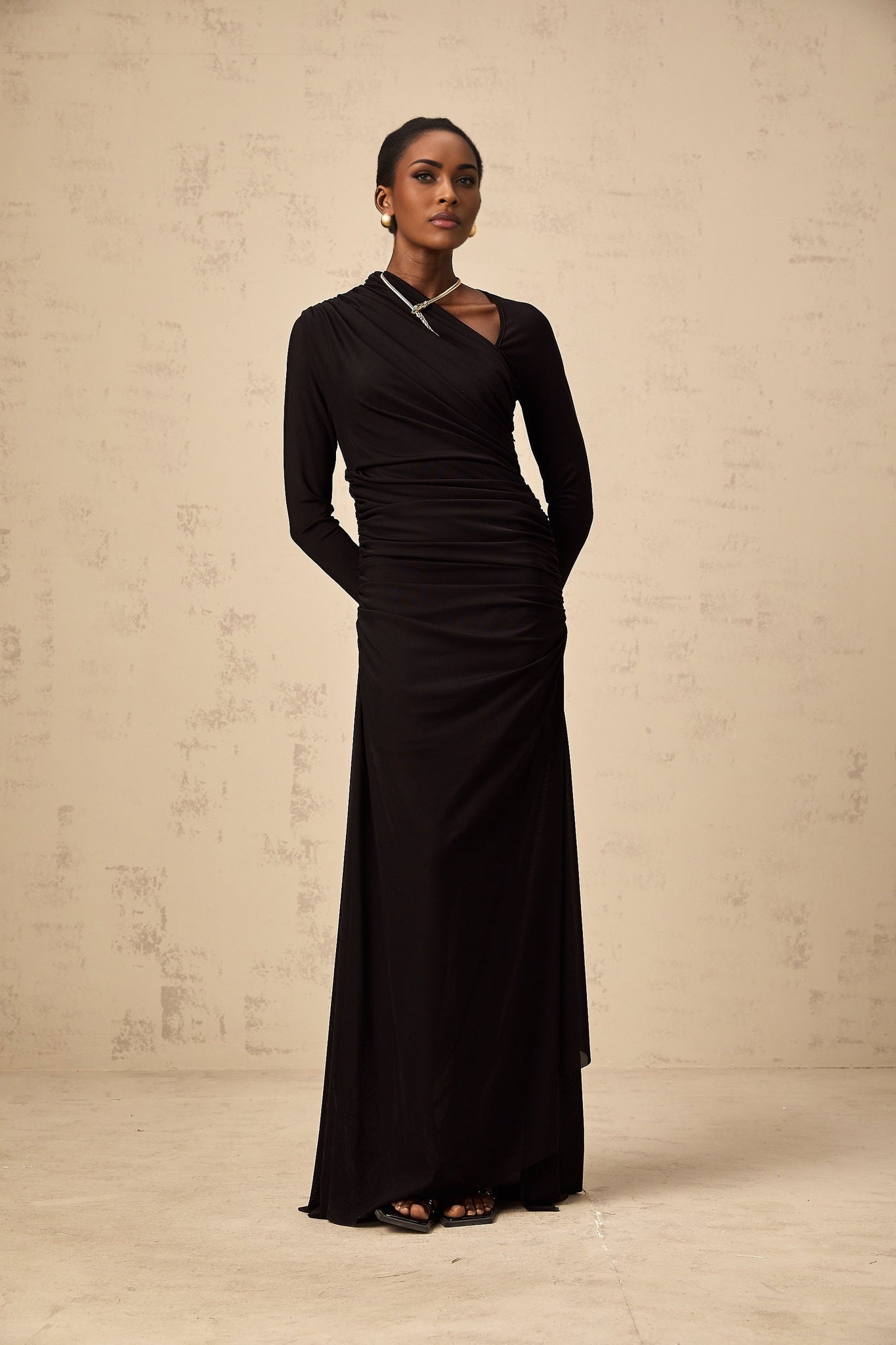 A black tulle maxi dress with asymmetric cutout details and an uneven hemline worn by a model against a plain background