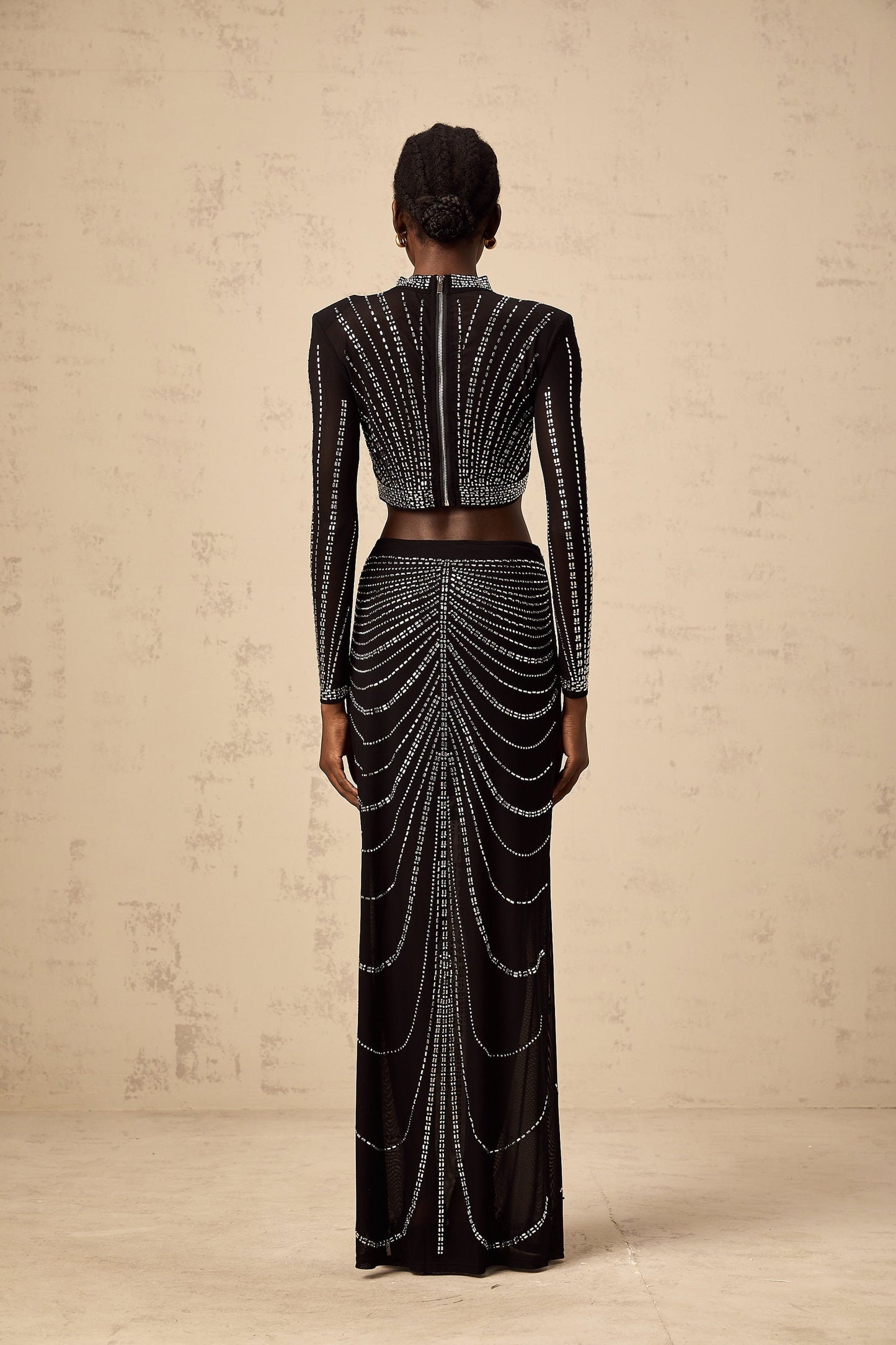 A black twopiece outfit consisting of a mesh top and skirt adorned with rhinestones The top has long sleeves and the skirt is knee length Both pieces feature a sparkly rhinestone pattern throughout the sheer mesh fabric