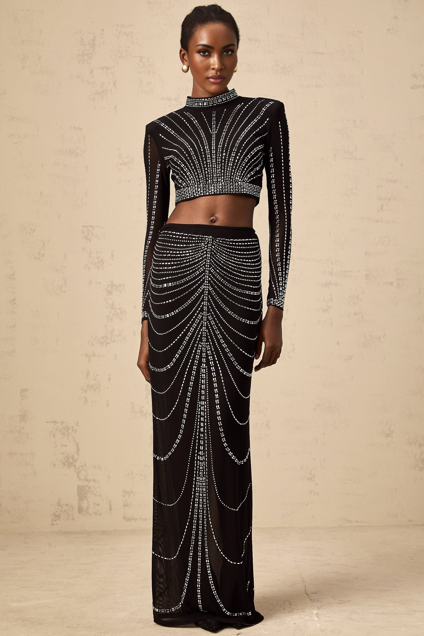 A black twopiece outfit consisting of a mesh top and skirt adorned with rhinestones The top is sleeveless with a high neckline The skirt is short and fitted Both pieces feature a sheer mesh material with sparkling rhinestone embellishments throughout