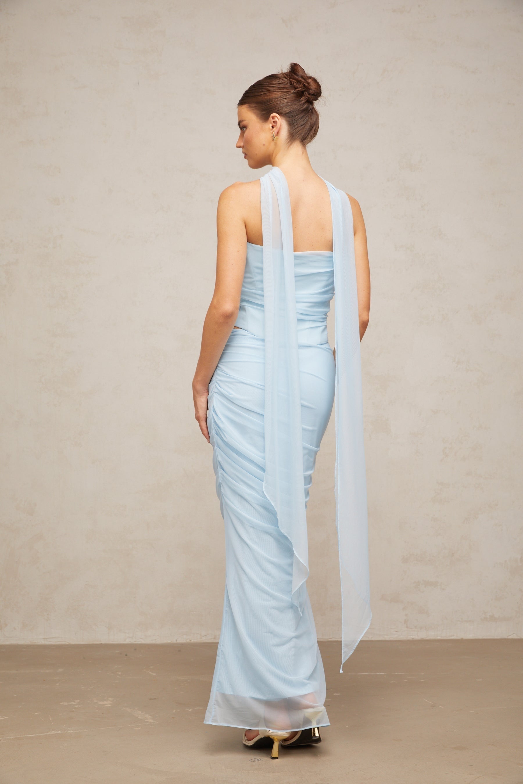 A blue matching set consisting of a ruched tulle top and skirt worn by a model against a plain background