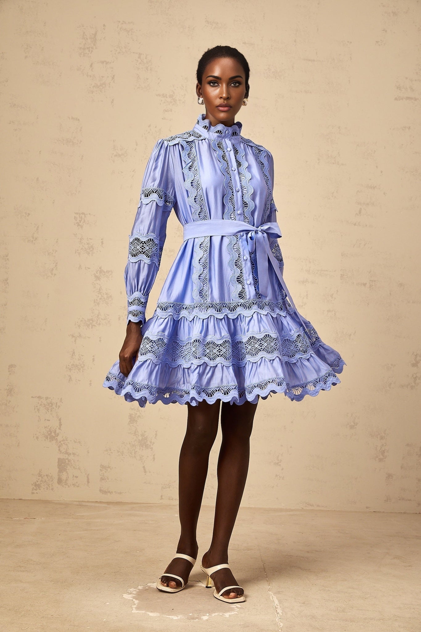 A blue mini dress with tiered layers and cut out embroidery details featuring a floral motif pattern throughout the fabric