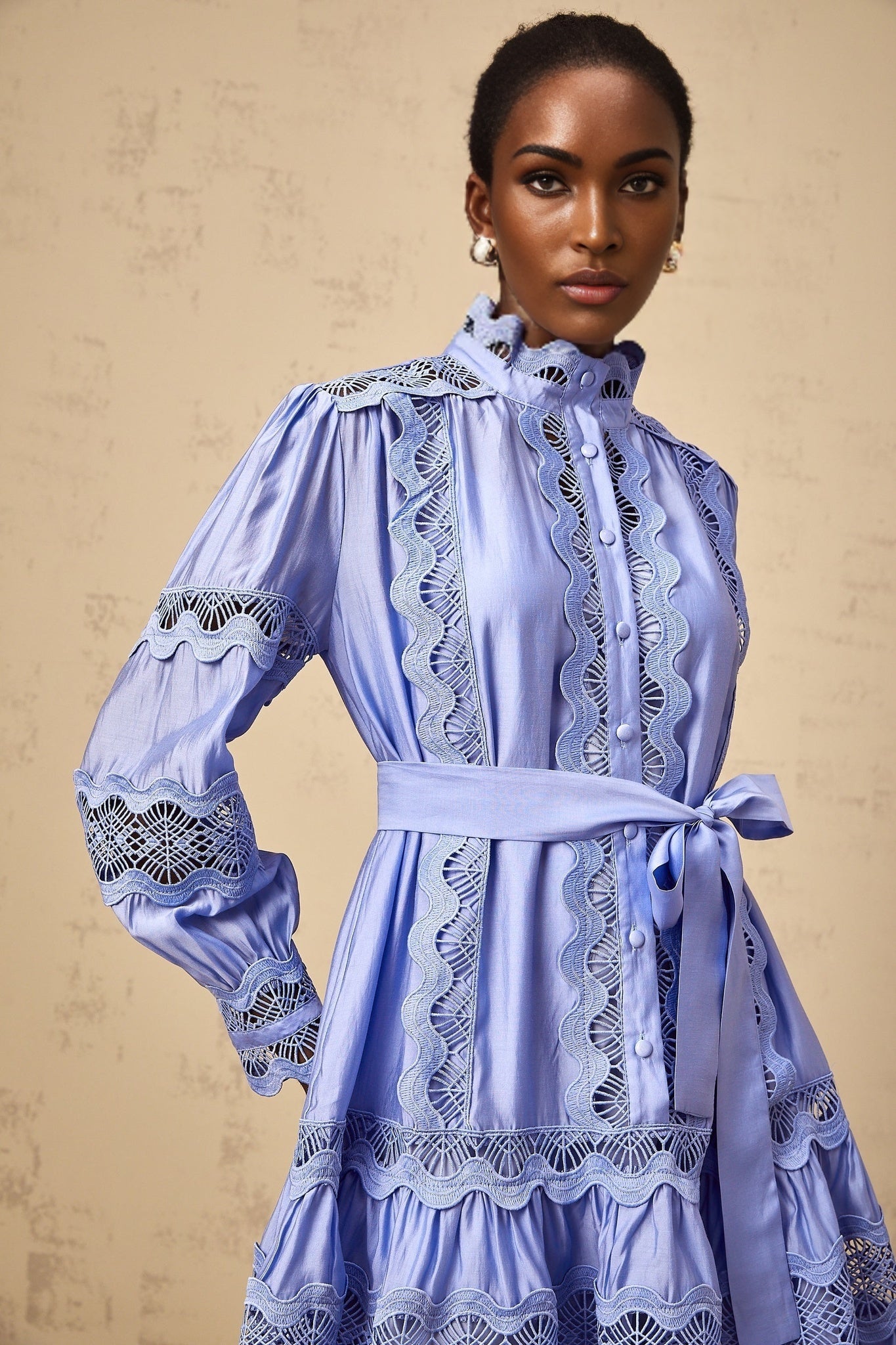 A blue mini dress with tiered layers featuring cutout embroidered motifs throughout the fabric