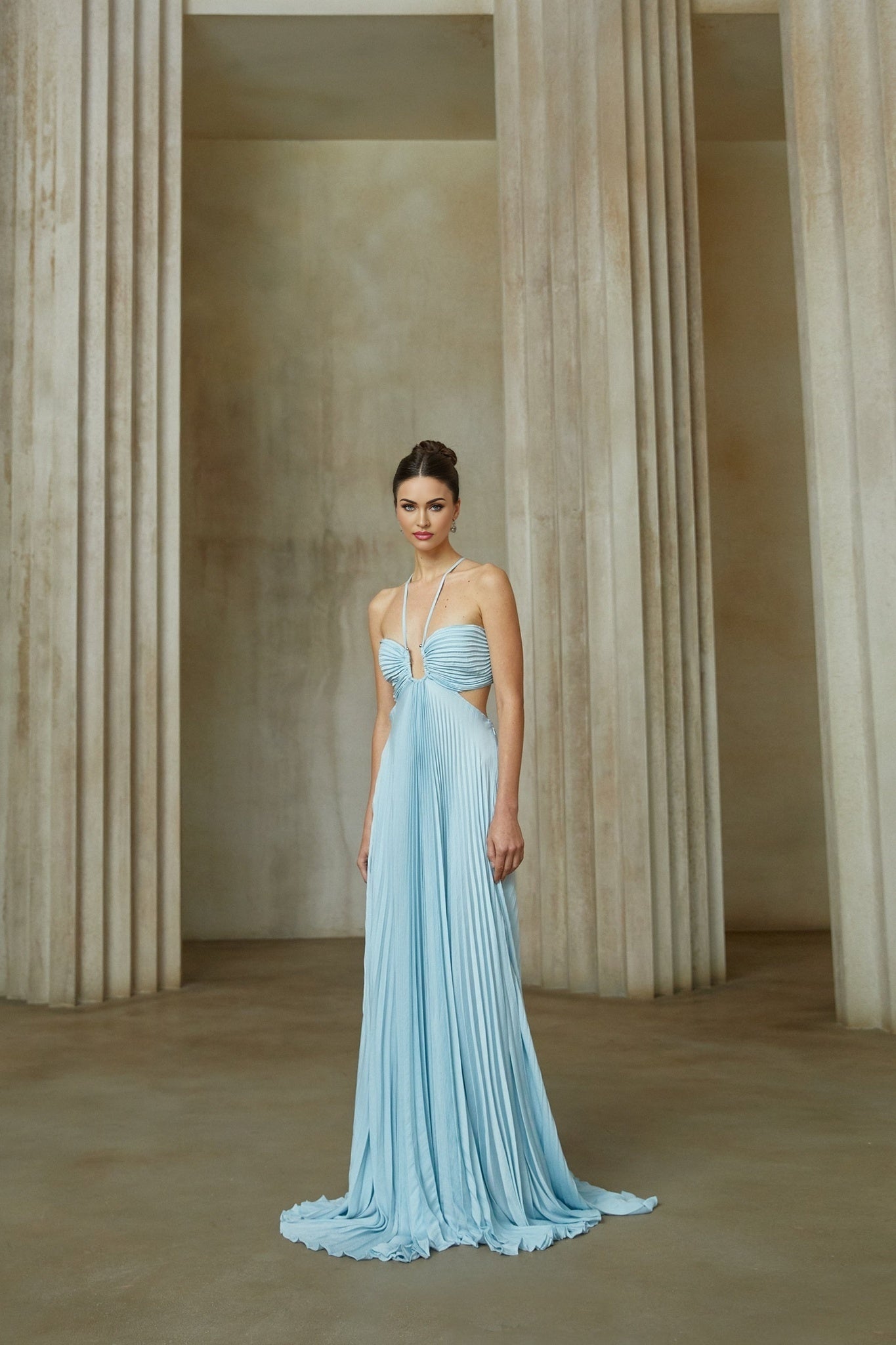 A blue pleated maxi dress with a cutout detail named Andrea worn by a model standing against a plain background