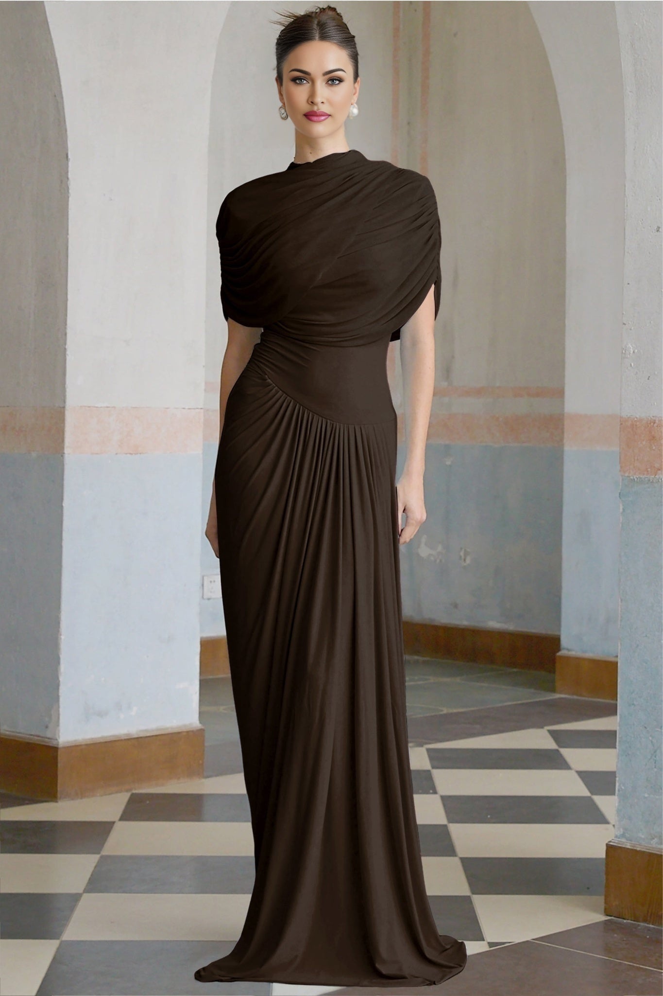 A brown asymmetric maxi dress with pleats and a flowing skirt worn by a model standing against a plain background