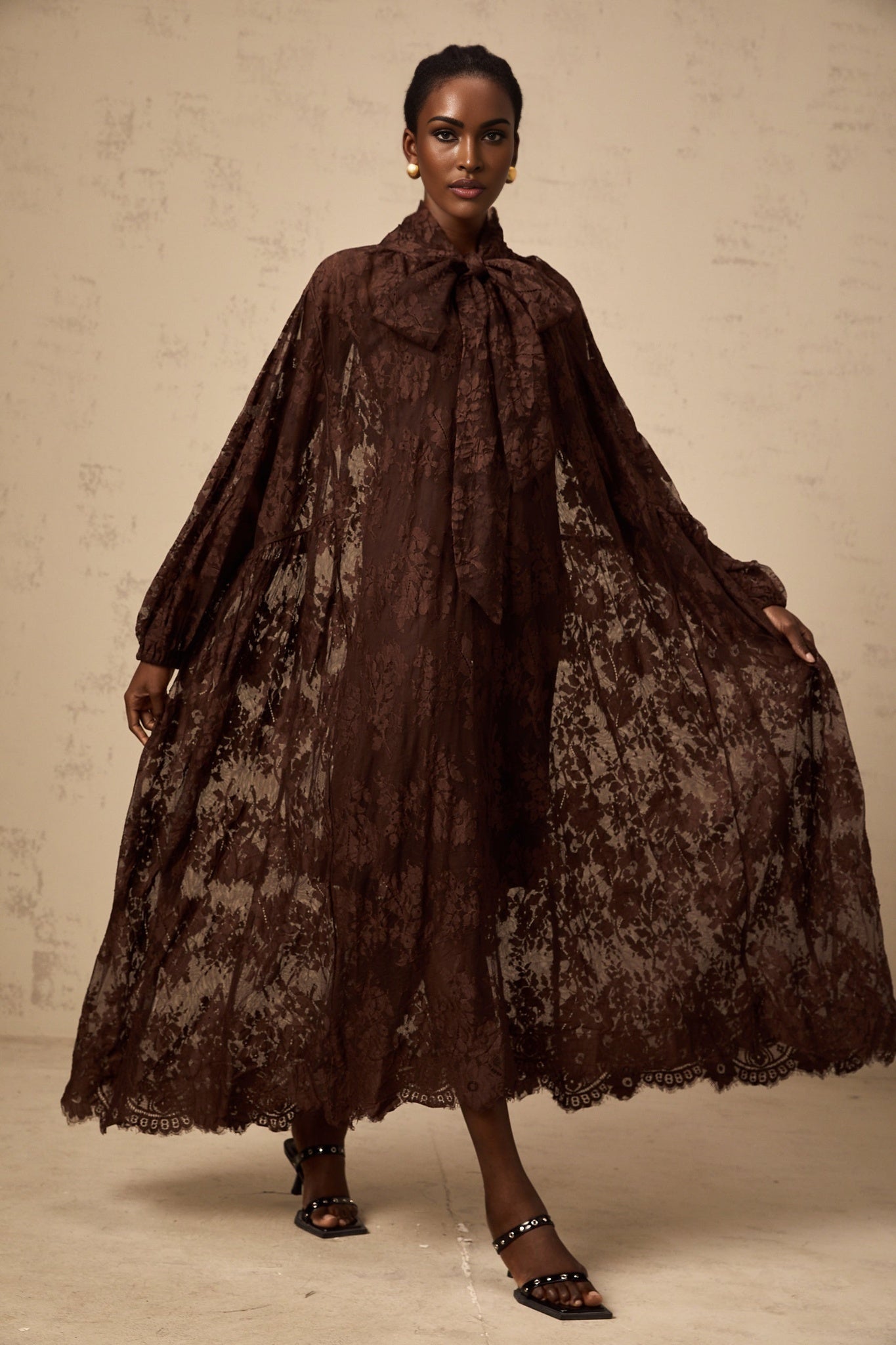 A brown flared midi dress made of chantilly lace named Sylvie on a plain background