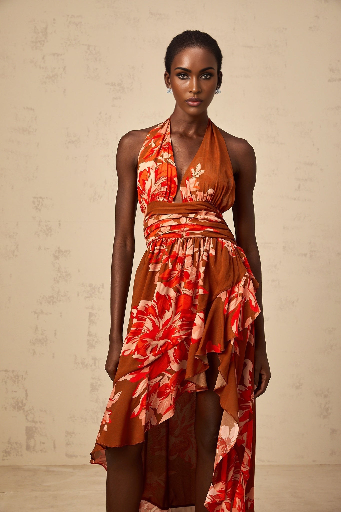 A brown maxi dress with a floral print pattern featuring an asymmetrical hemline and a flowing silhouette