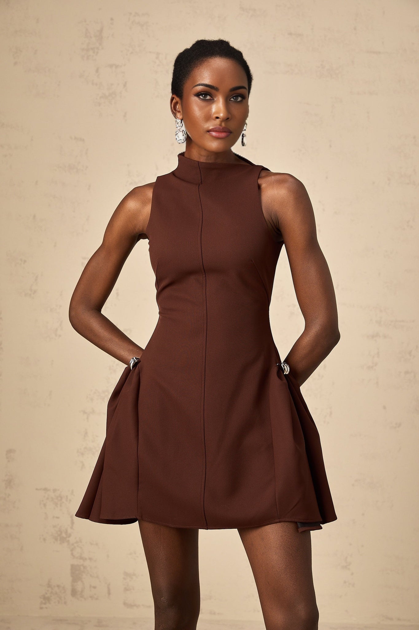 A brown mini dress with an asymmetric neckline and puff sleeves styled on a model named Dora