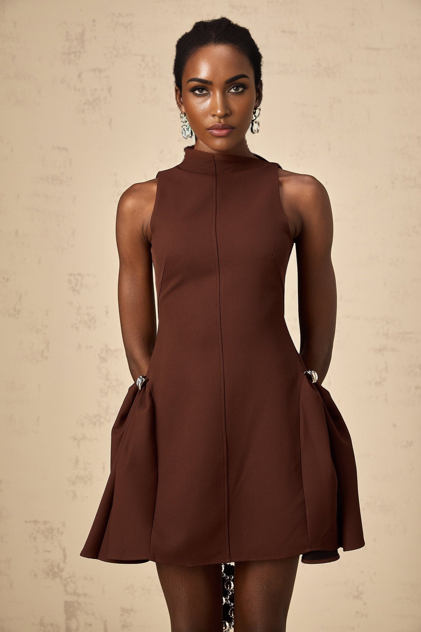 A brown mini dress with an asymmetric neckline and puff sleeves worn by a model named Dora