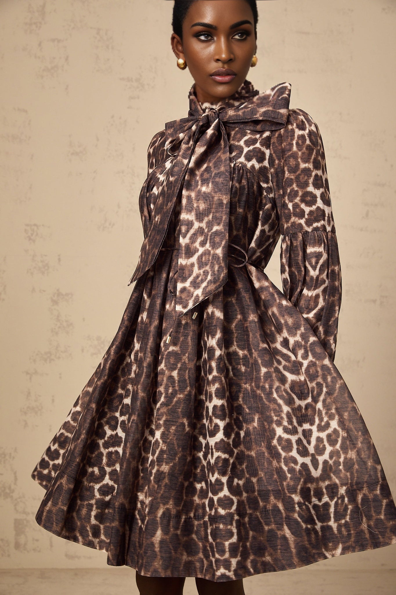 A brown mini dress with leopard print pattern featuring a bow detail at the waist and a short hemline