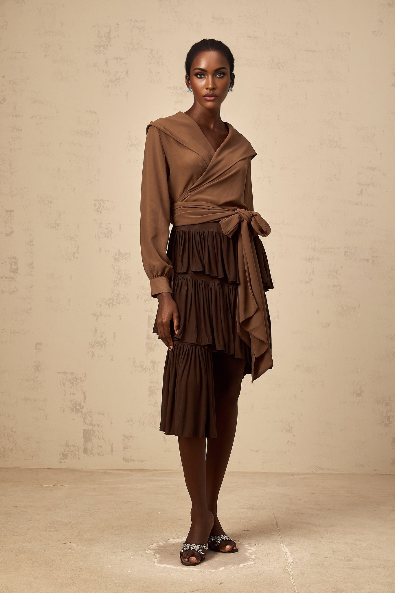 A brown mini skirt with asymmetrical design featuring pleated tiers and a flared silhouette named Astrid