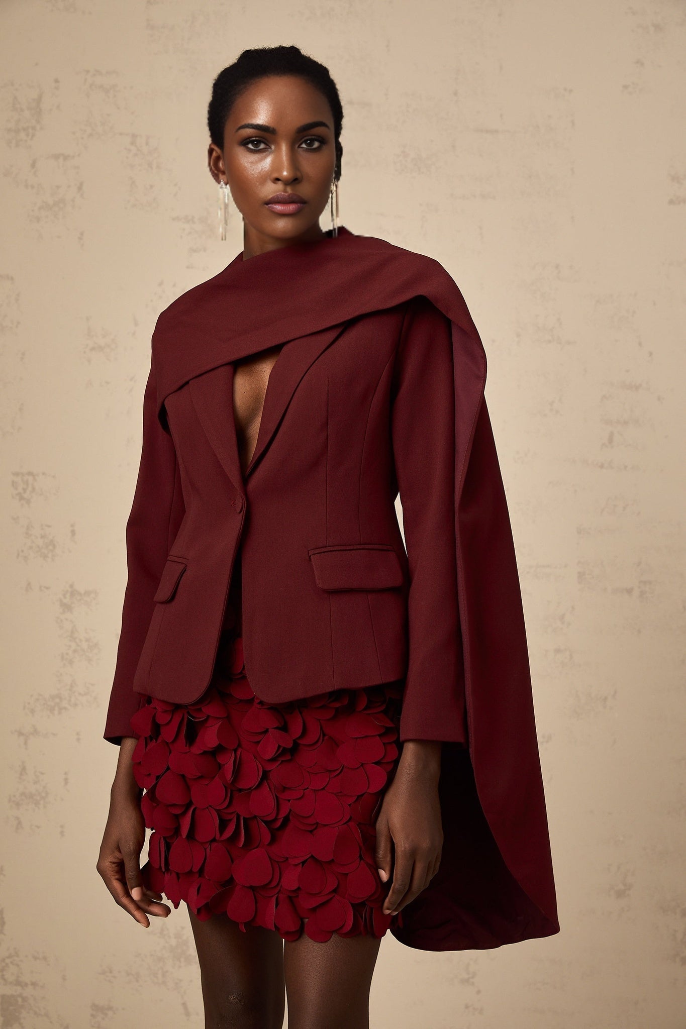 A burgundy colored jacket with a shawl collar and detailed design worn by a model against a plain background