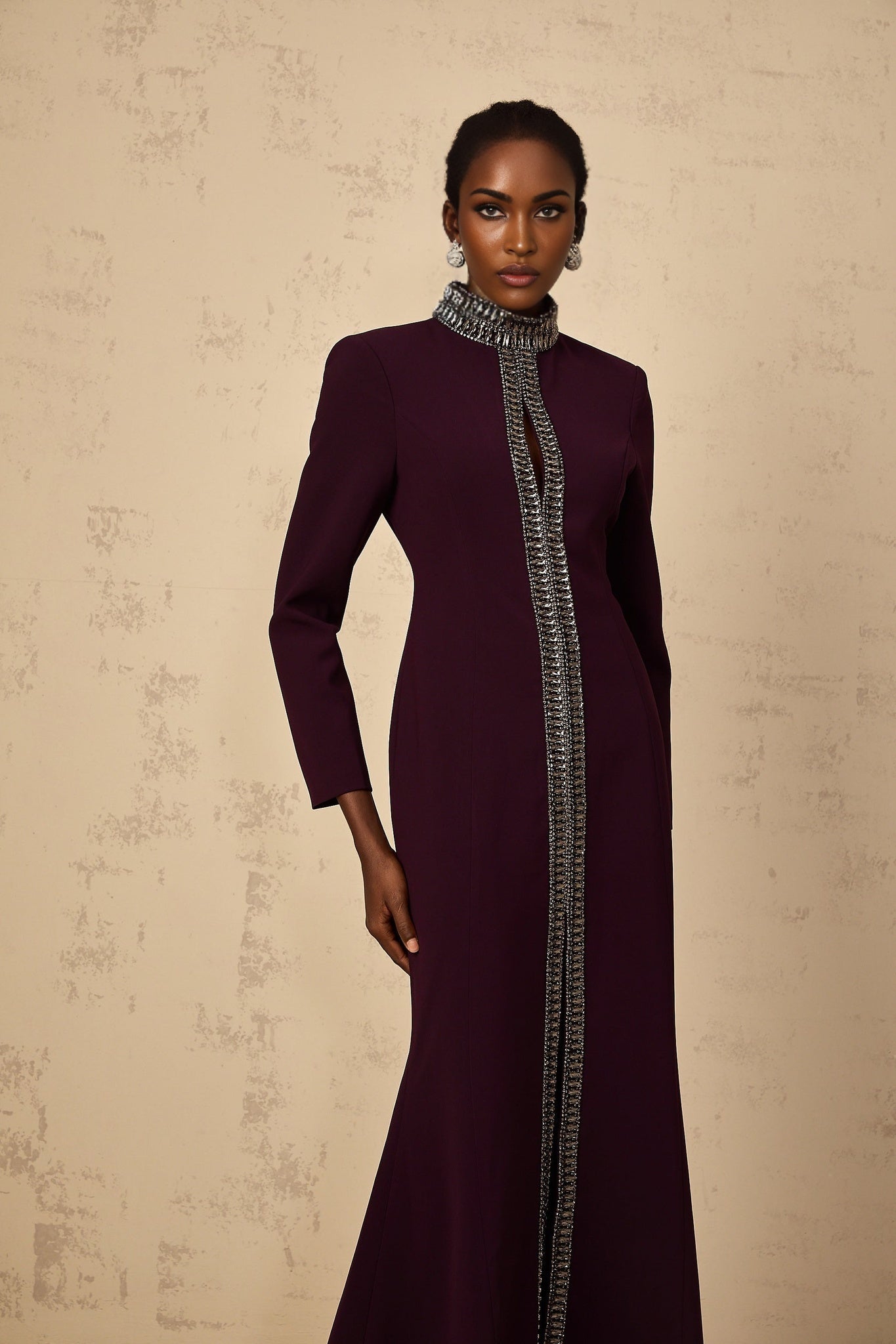 A burgundy floorlength maxi dress with a flared silhouette and embellished details worn by a model against a plain background