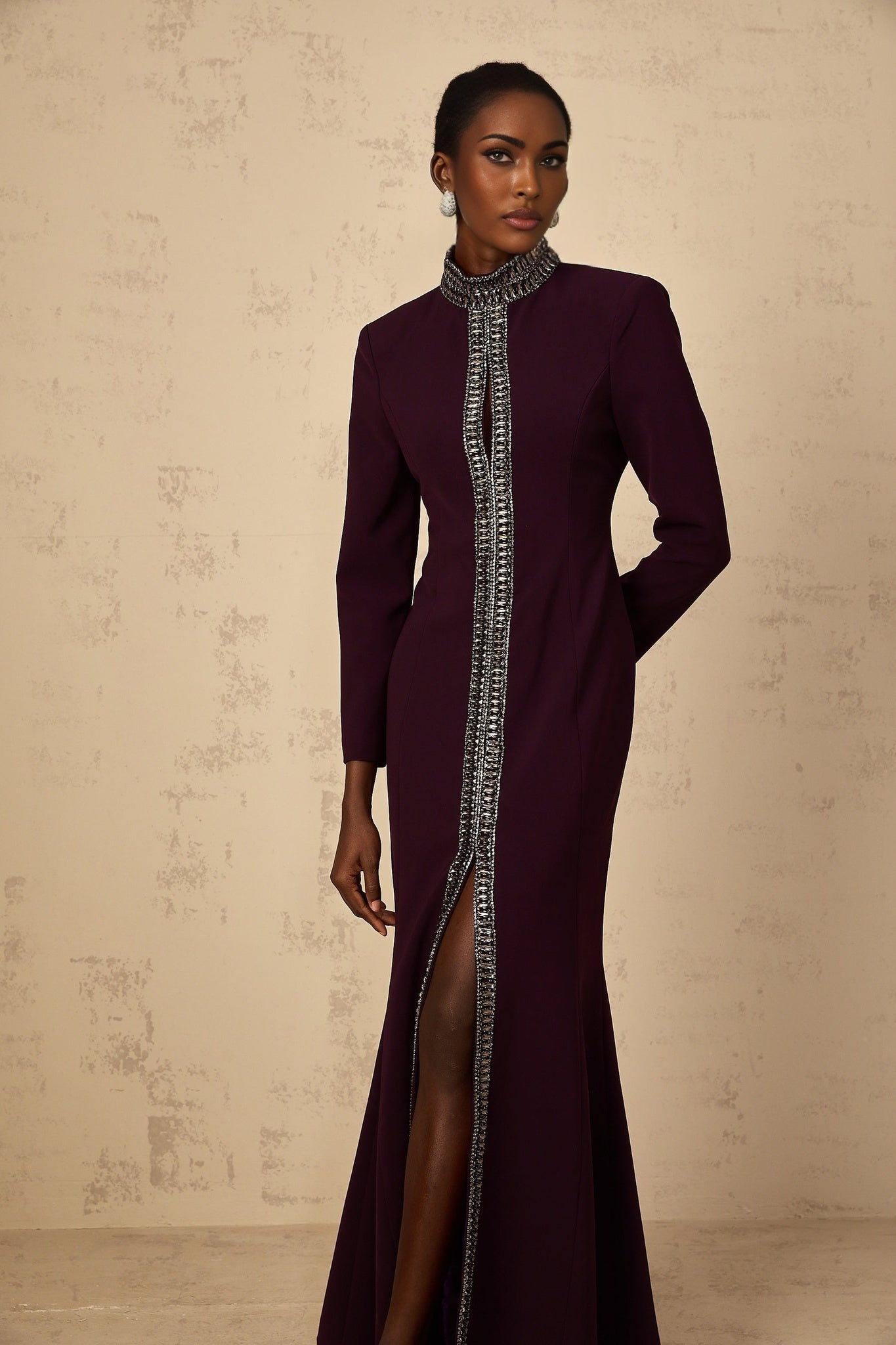 A burgundy floorlength maxi dress with a flared skirt and embellished details worn by a model against a plain background