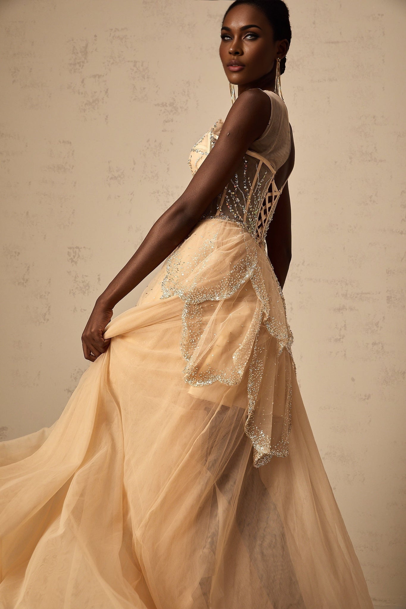 A champagne colored gown with a highlow hemline featuring daisy embellishments and a flowing silhouette