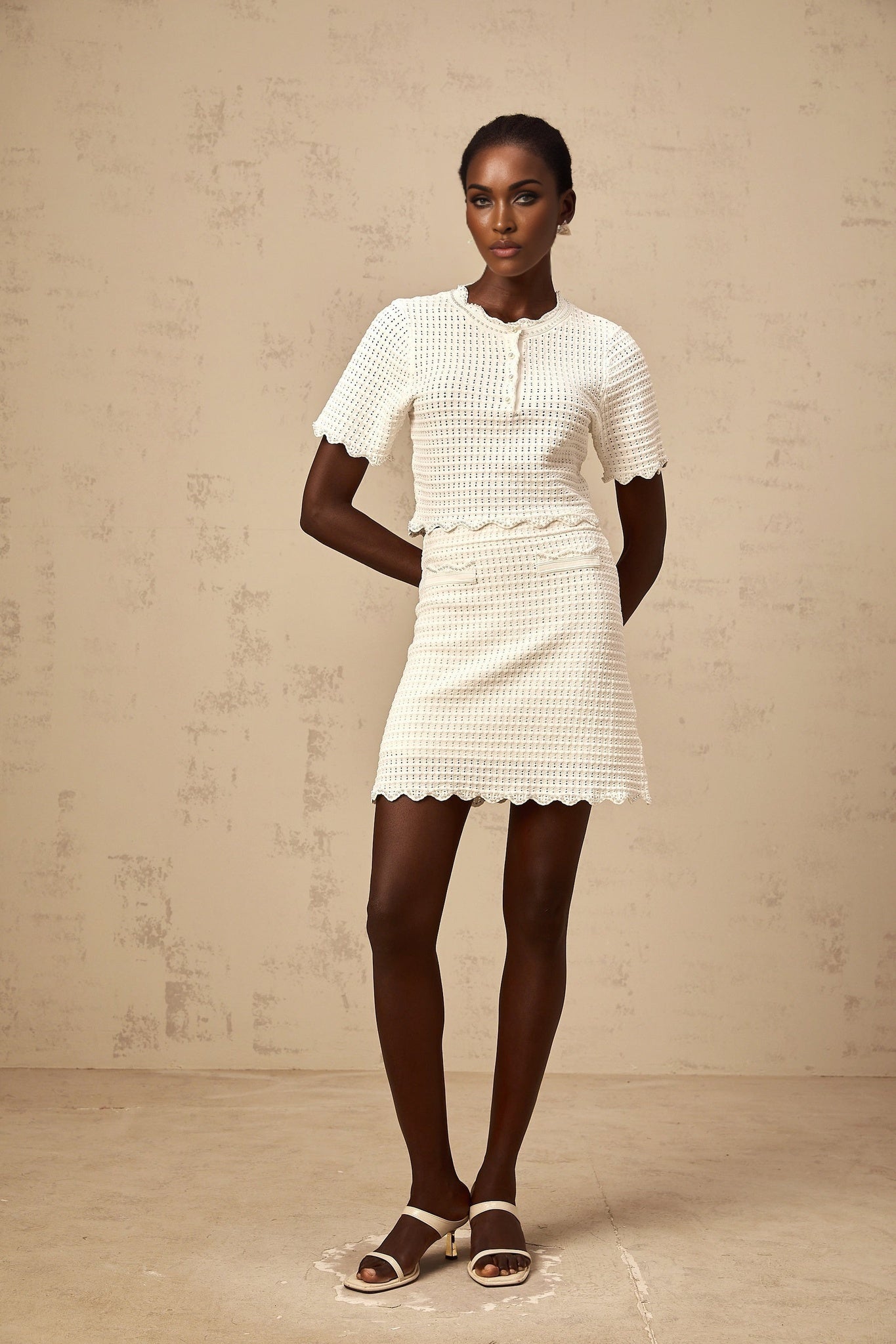 A creamwhite matching set consisting of a ruffled top and skirt made from pointelle knit fabric The top features a delicate ruffled design while the skirt complements with a similar texture Both pieces are designed in a light cream color