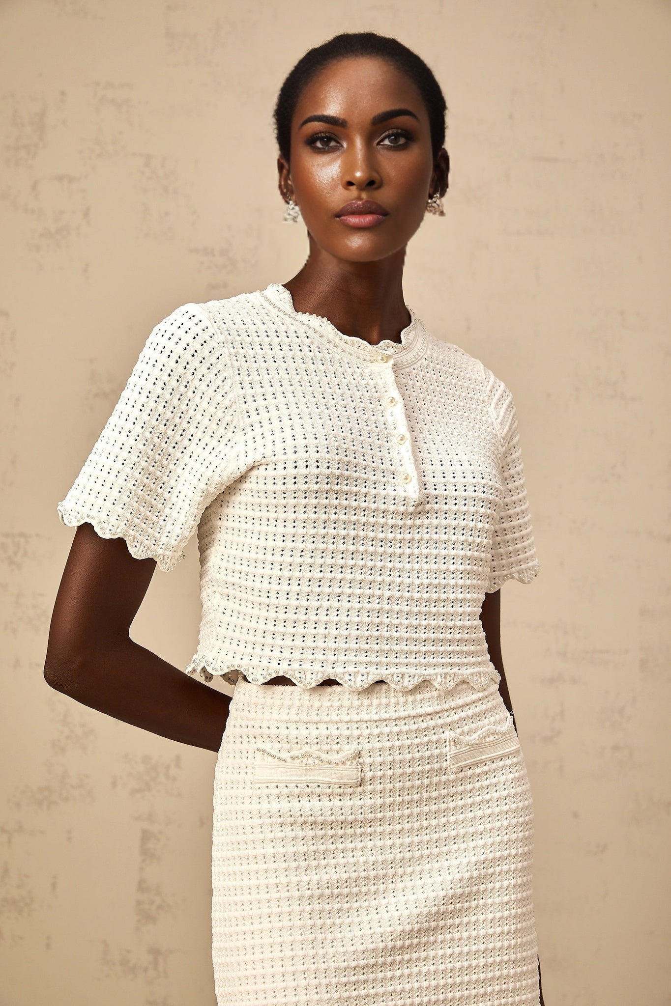 A creamwhite matching set featuring a ruffled top and skirt both made of pointelle knit fabric The top has a delicate ruffled design while the skirt complements it with a similar texture and color