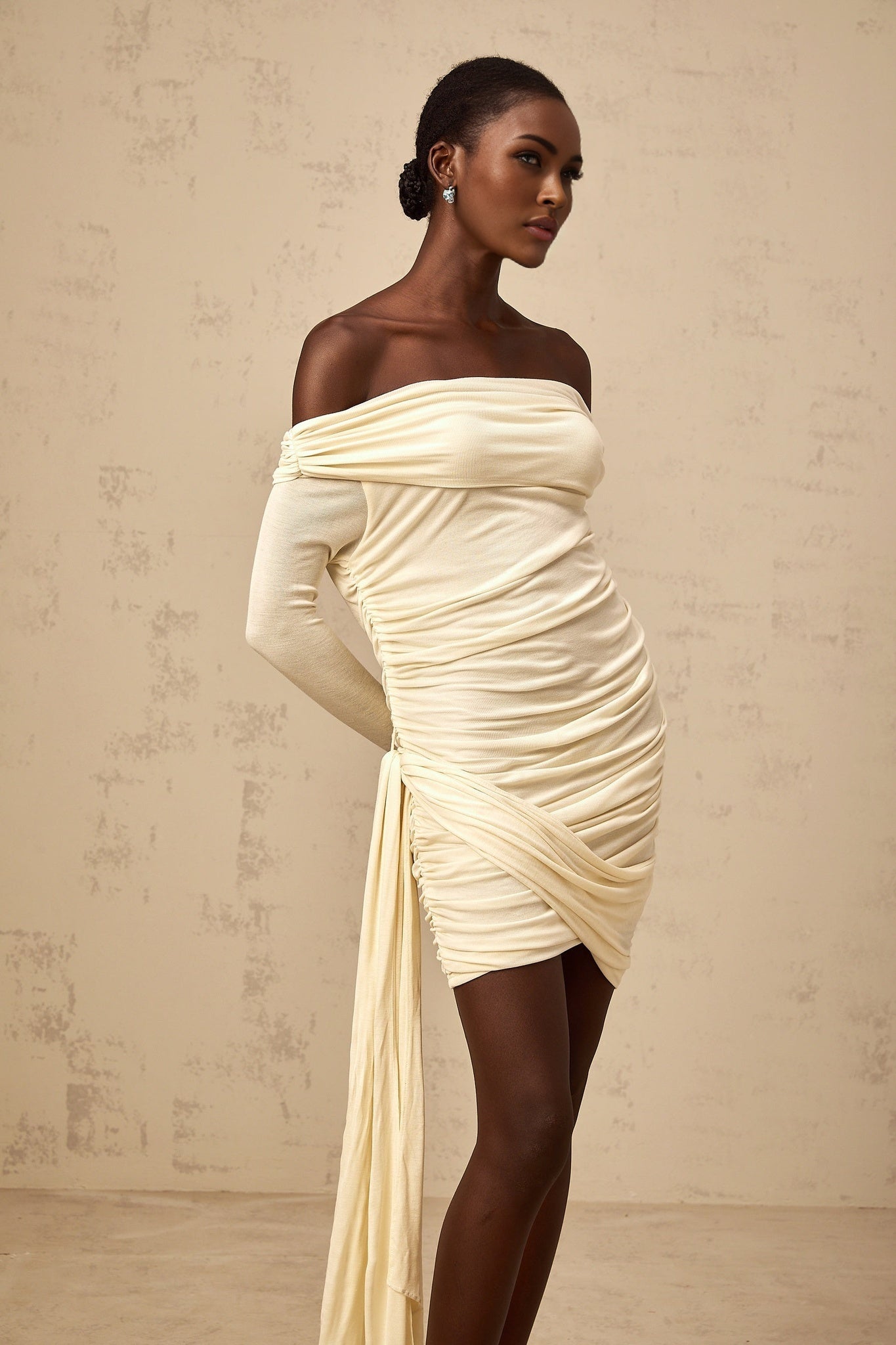 A creamwhite mini dress with ruched fabric and ribbon design details named Margaux