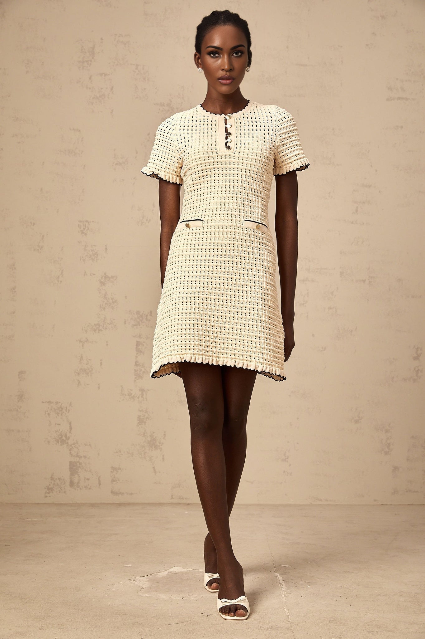 A feminine neutralcolored mini dress with ruffled details and pointelle knit fabric featuring a short length and delicate pattern