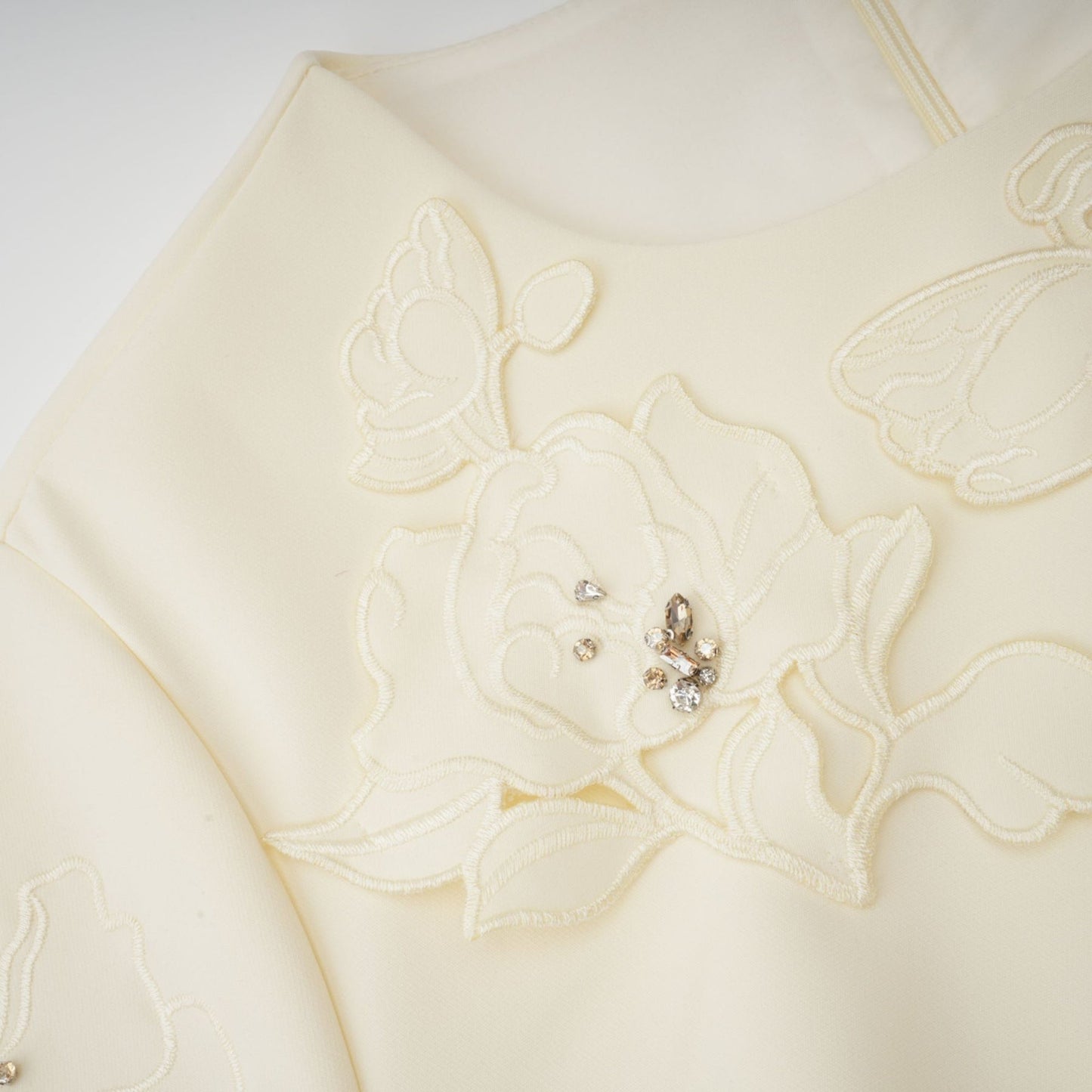 A flared midi dress in neutral tones featuring floral applique details with a predominantly orange color scheme