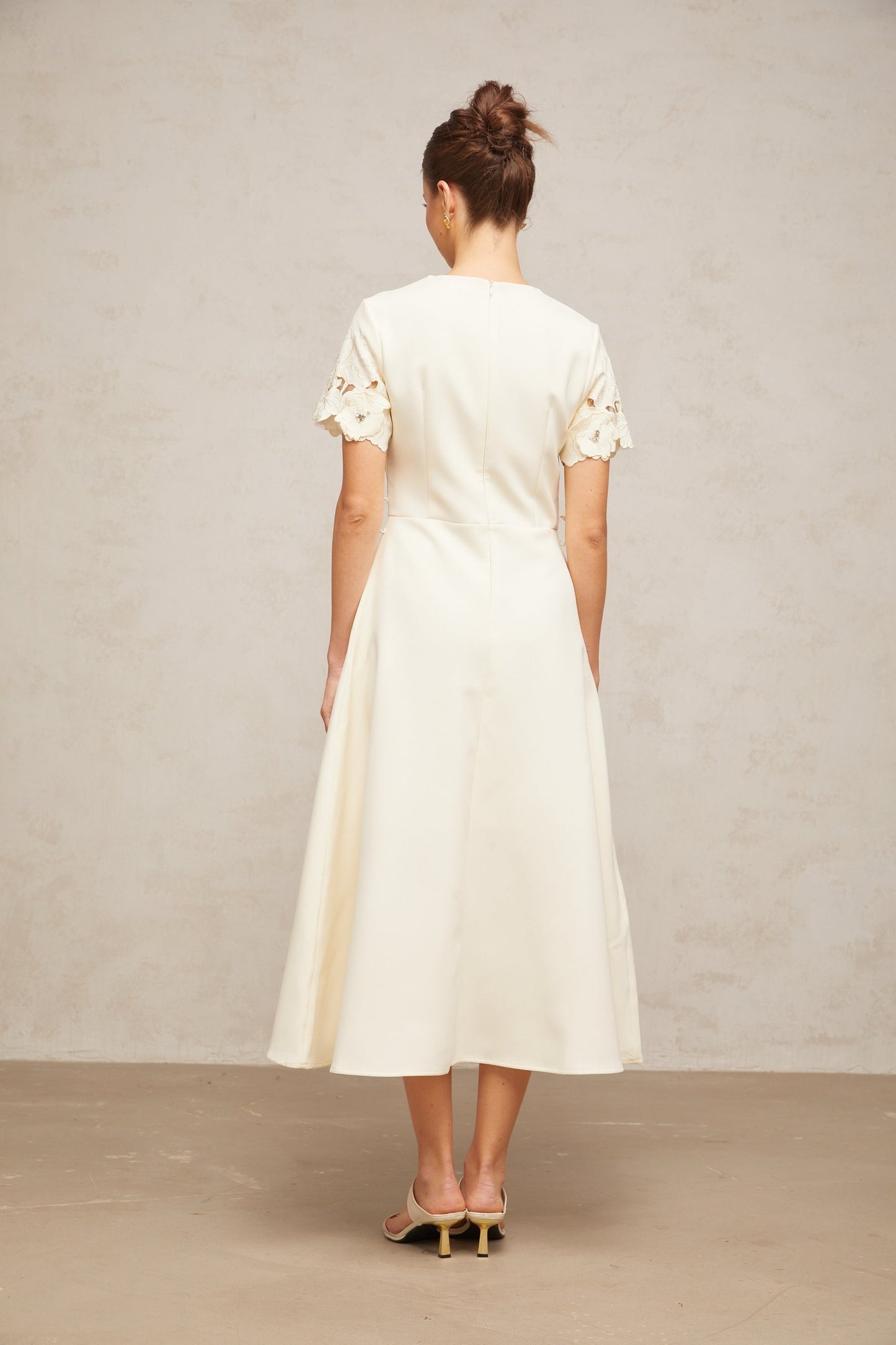 A flared midi dress in neutral tones featuring orange floral appliqués decorating the fabric with a feminine and elegant design
