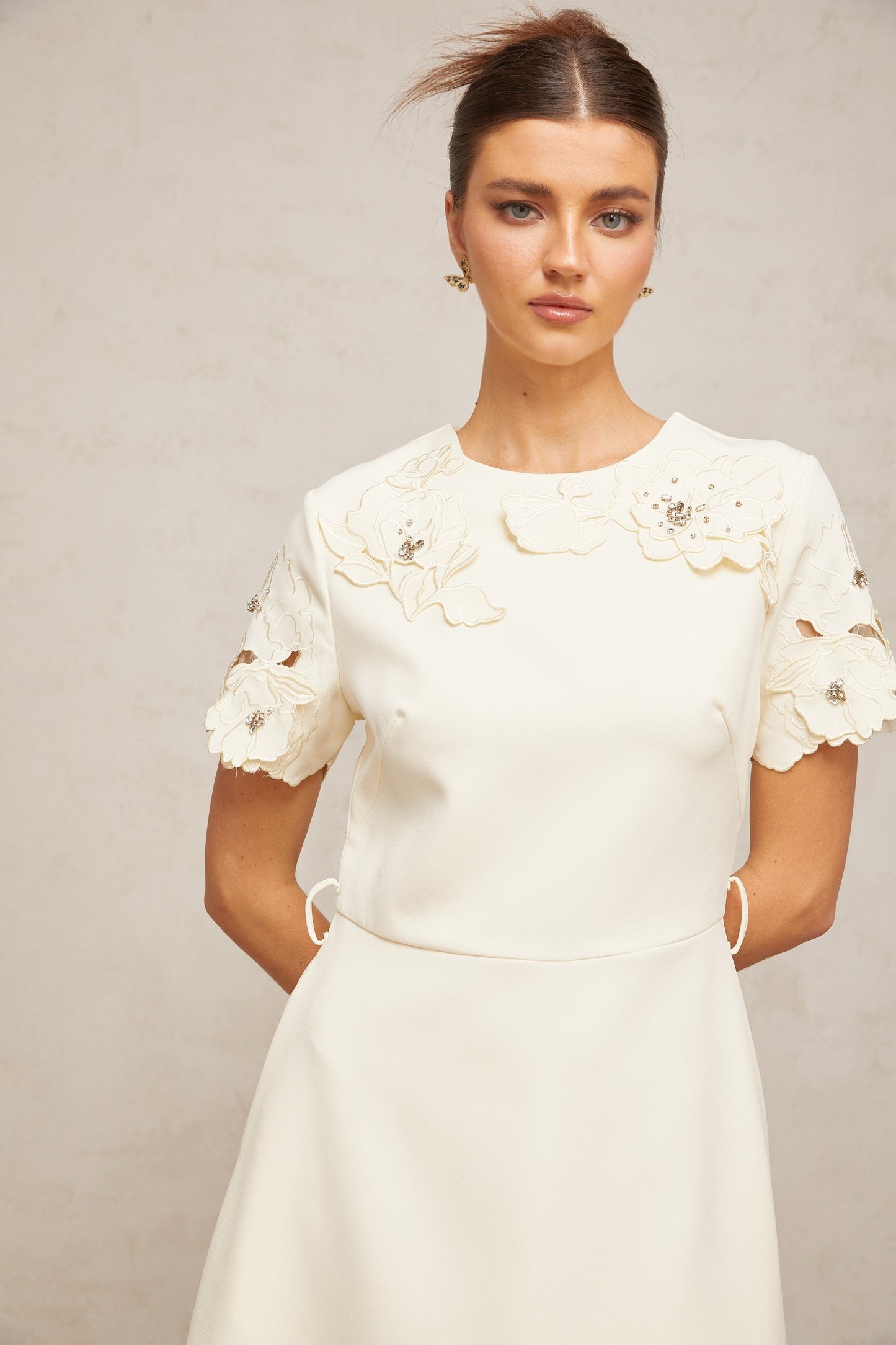 A flared midi dress in neutral tones featuring orange floral appliqués on the fabric